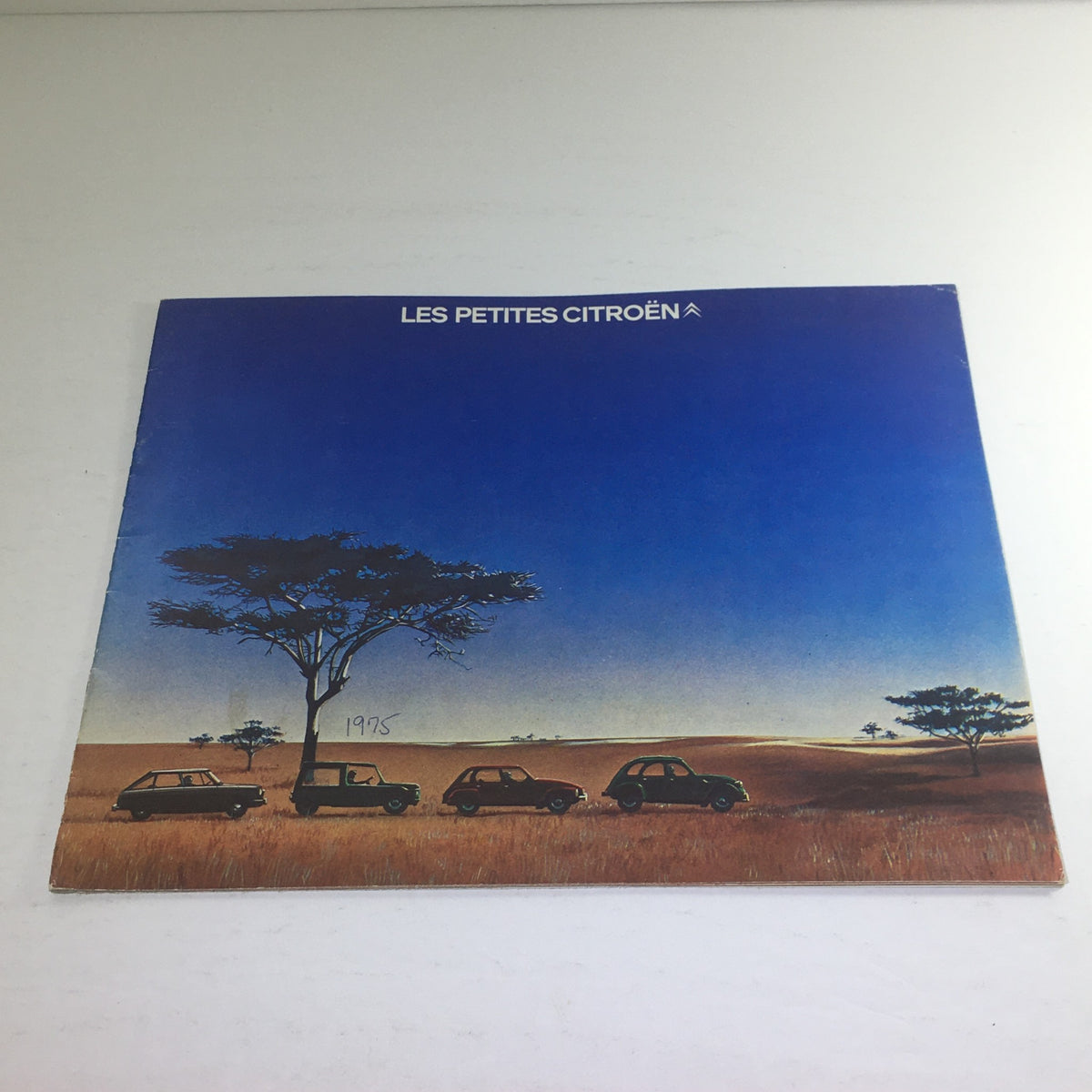 Cover of the 1975 Les Petites Citroen 2 CV 6 (French) Dealership Car Auto Brochure Catalog featuring a scenic landscape with four Citroen cars under a blue sky.