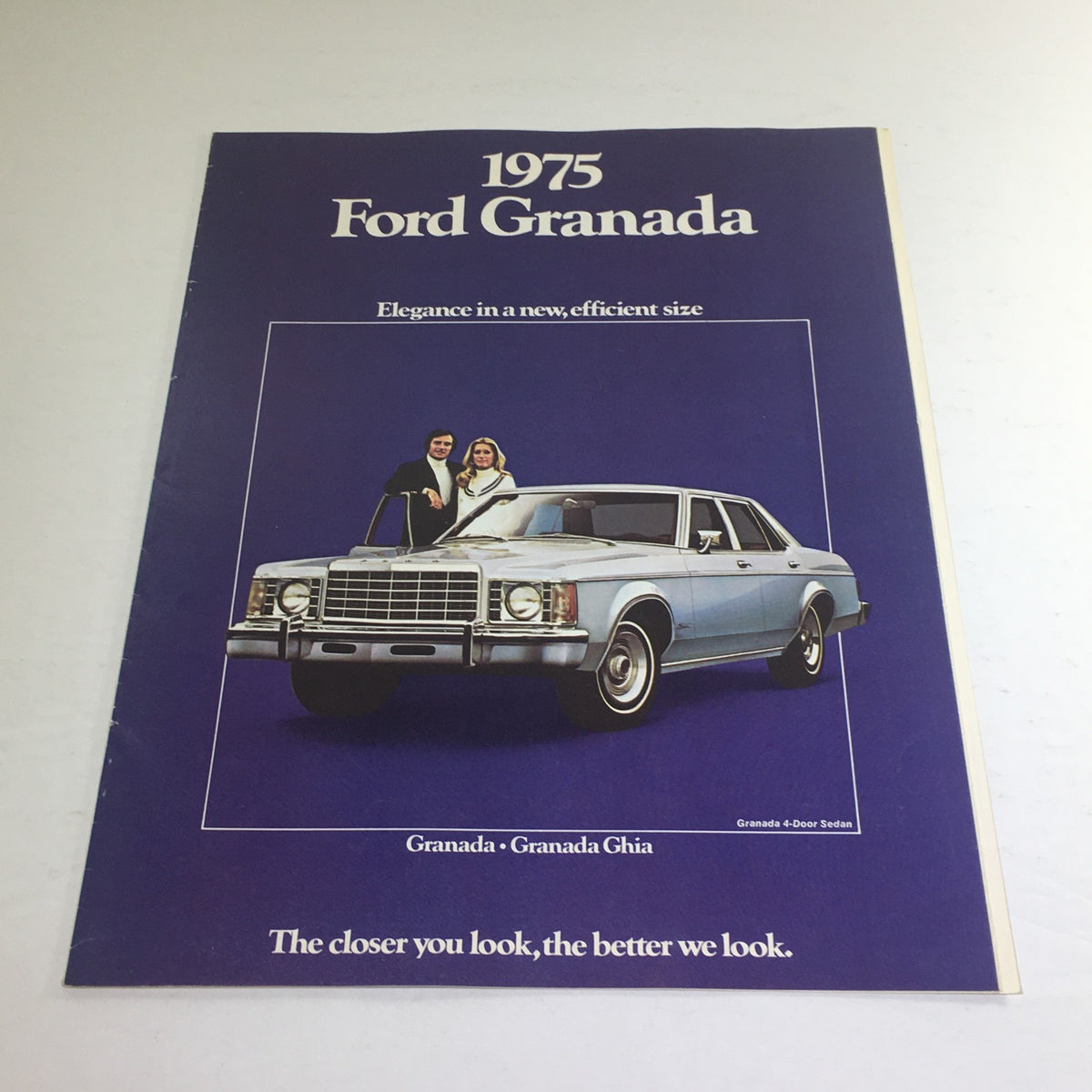 1975 Ford Granada Ghia Sedan specification brochure cover with a couple beside the car, featuring a blue color scheme and the tagline 'The closer you look, the better we look.'
