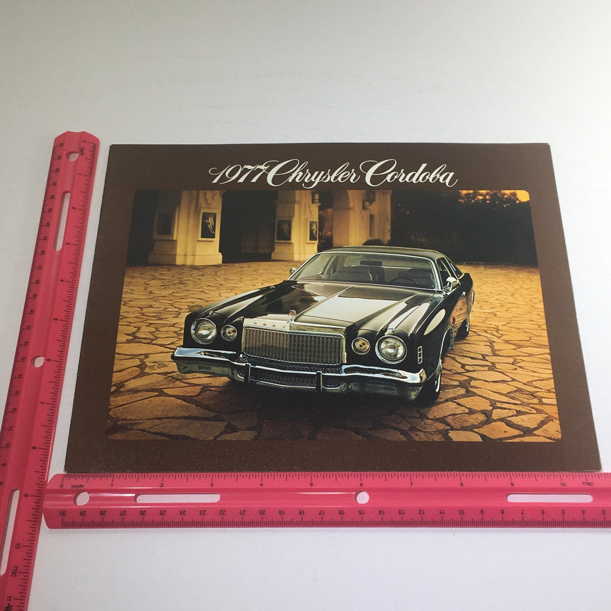 Image of a 1977 Chrysler Cordoba with a ruler for scale, emphasizing its classic design in the 1977 Chrysler Cordoba Halo Roof Dealership Car Auto Brochure Catalog.