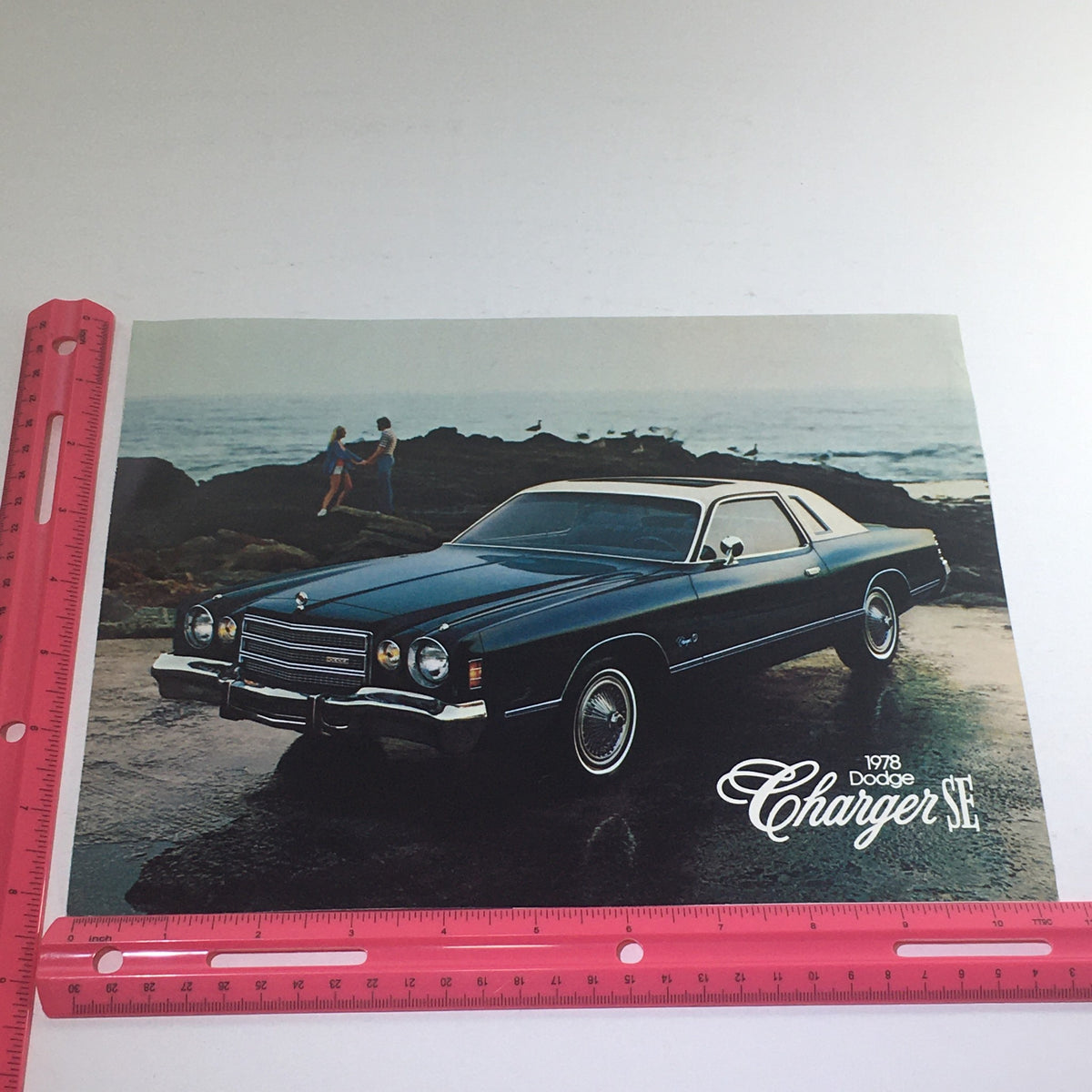 Front view of a 1978 Dodge Charger SE Sedan on a rocky beach, highlighted in a dealership catalog photo.