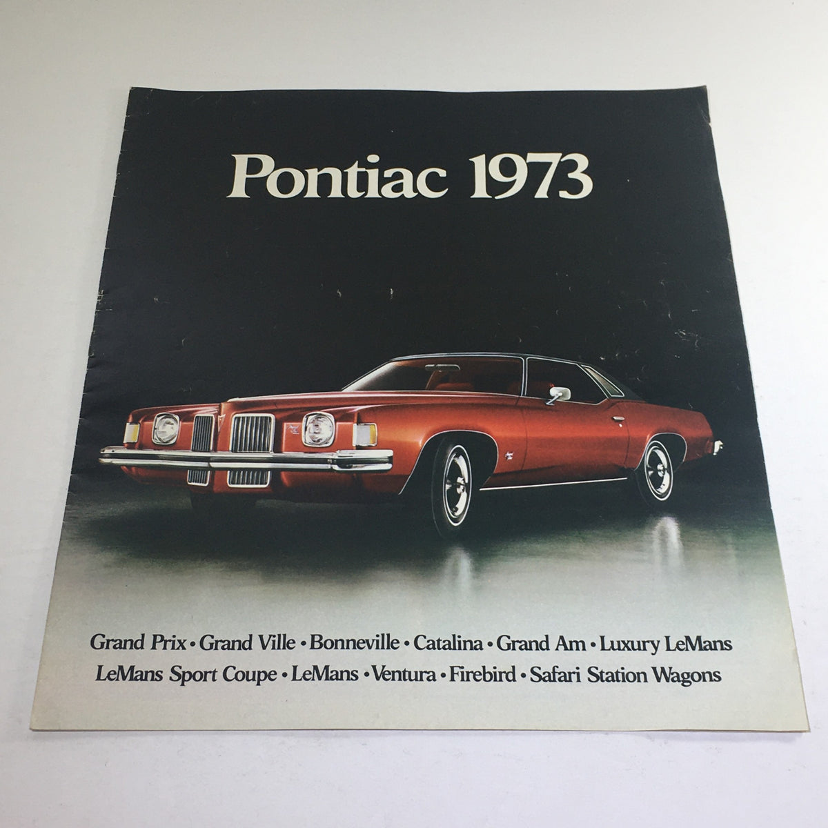 1973 Pontiac Grand Prix & Ville/Bonneville Dealership Car Auto Brochure Catalog featuring a stylish red Pontiac vehicle with prominent grille and headlights, showcasing the model lineup for Pontiac in 1973.