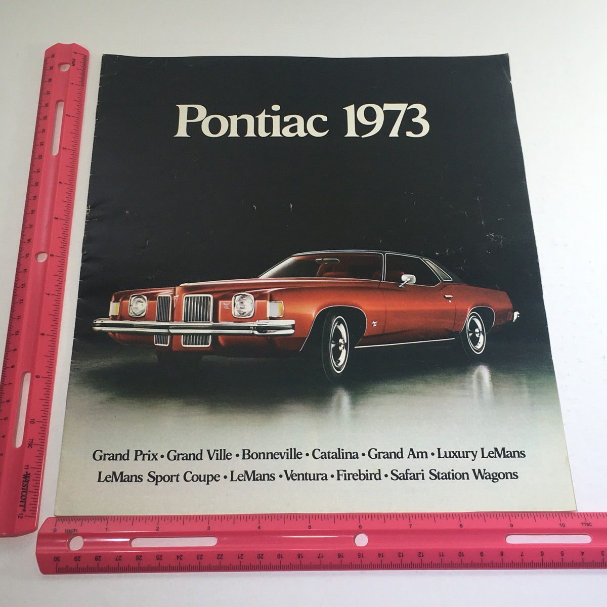 Front cover of the 1973 Pontiac Grand Prix & Ville/Bonneville Dealership Car Auto Brochure Catalog featuring a red Pontiac vehicle and various Pontiac models listed.