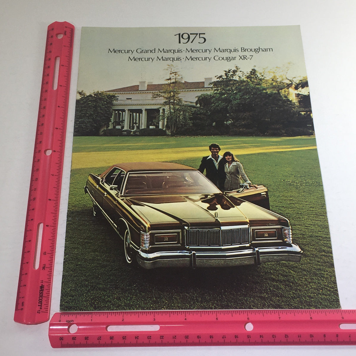 Measuring the cover of the 1975 Ford Mercury Grand Marquis/Cougar XR-7 Dealership Car Auto Brochure Catalog with a pink ruler for size reference.