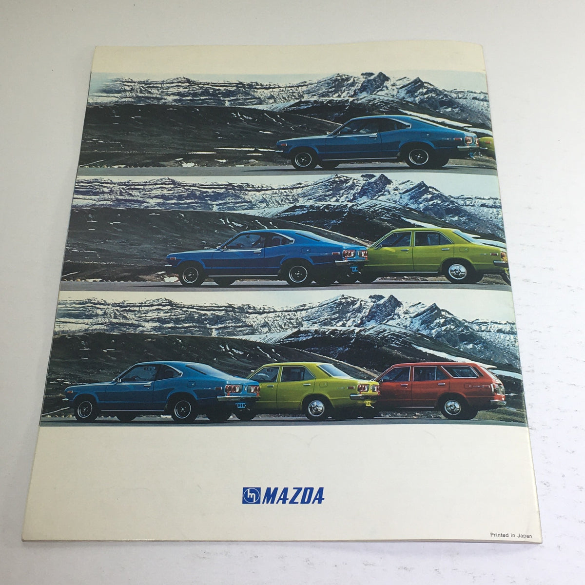 Back cover of the 1973 Mazda RX-3 Coupe Sedan Station Wagon Dealership Car Auto Brochure featuring Mazda RX-3 cars parked against a mountainous backdrop.