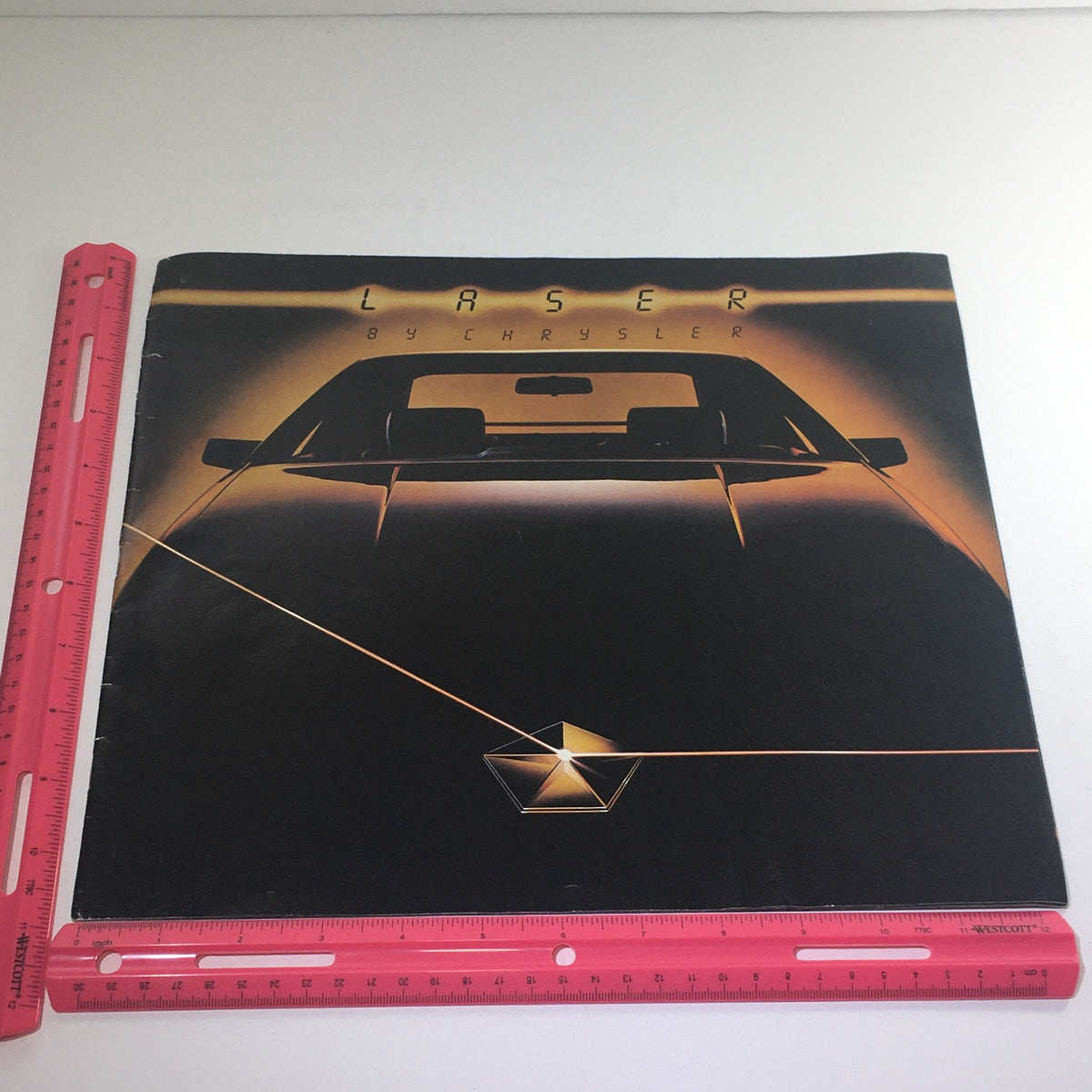 1984 Laser XE by Chrysler brochure cover with a ruler for size reference, highlighting its dimensions.