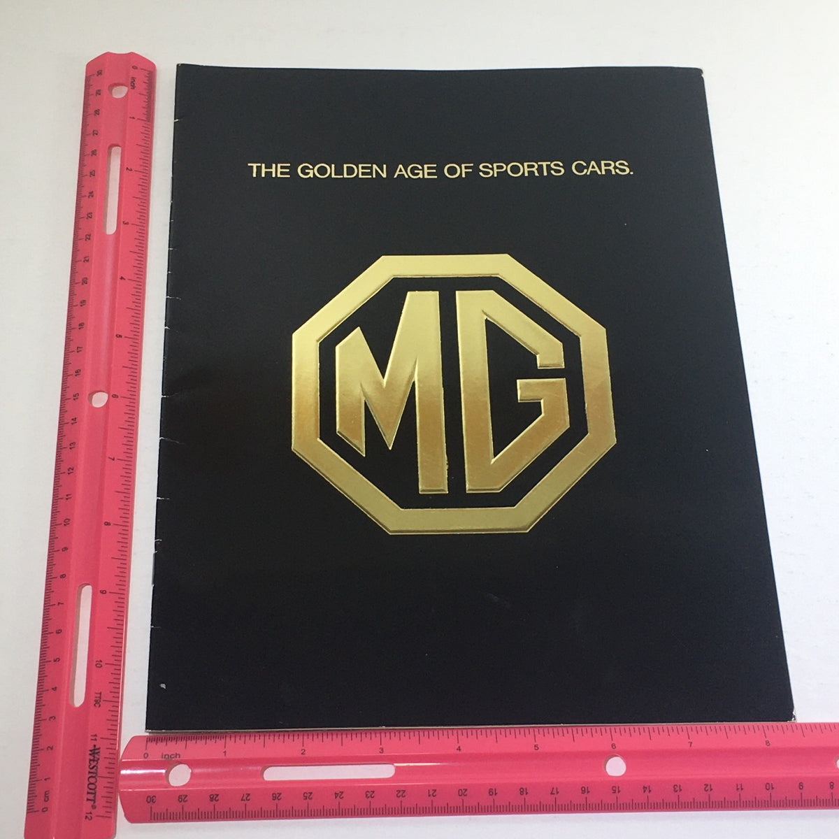 Side view of the 1975 MG Sports Car Dealership Car Auto Brochure Catalog with a ruler for scale, highlighting its size and design.