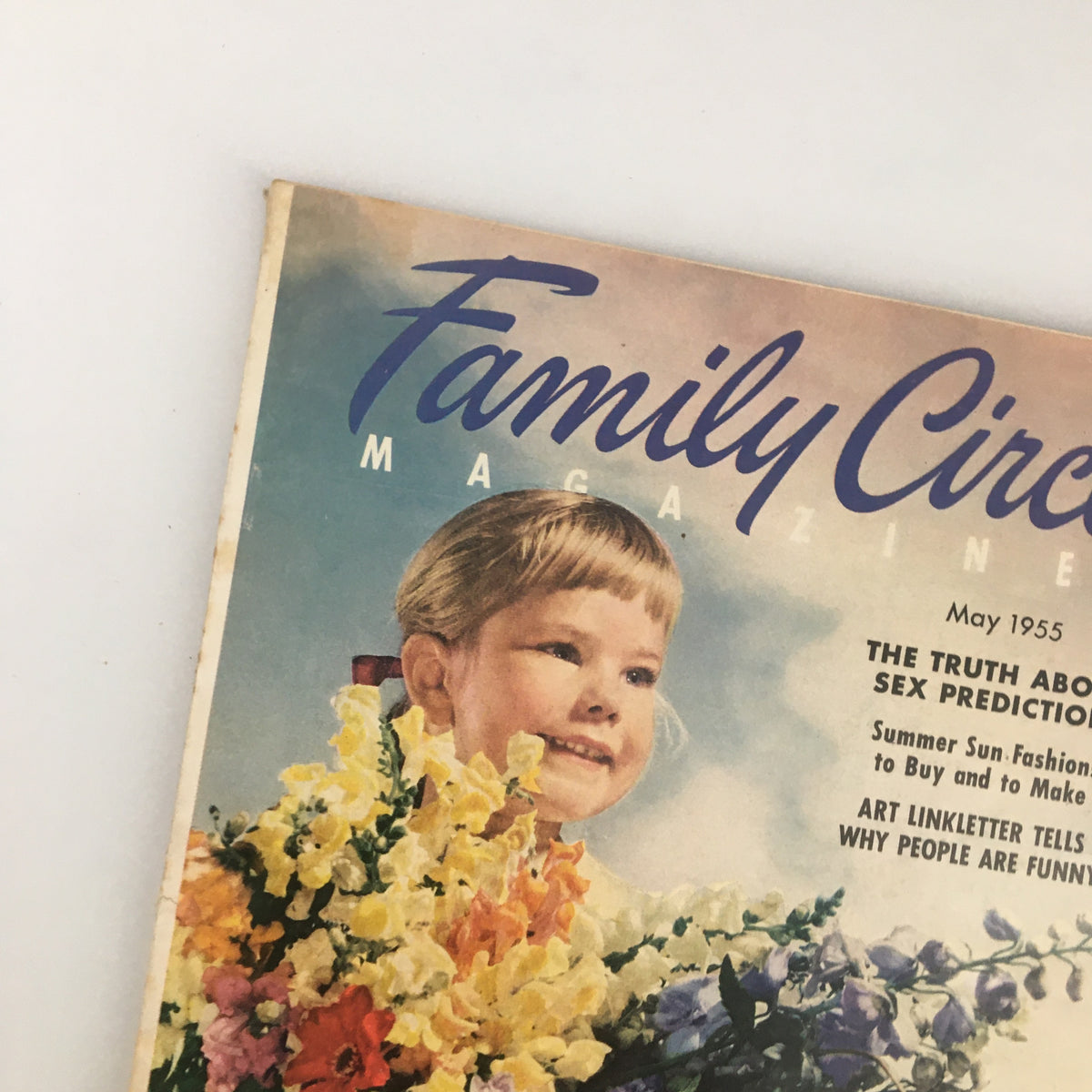 Close-up of the cover of VTG Family Circle Magazine May 1955 showcasing a smiling girl surrounded by colorful flowers, representing the nostalgic essence of mid-20th century family traditions.