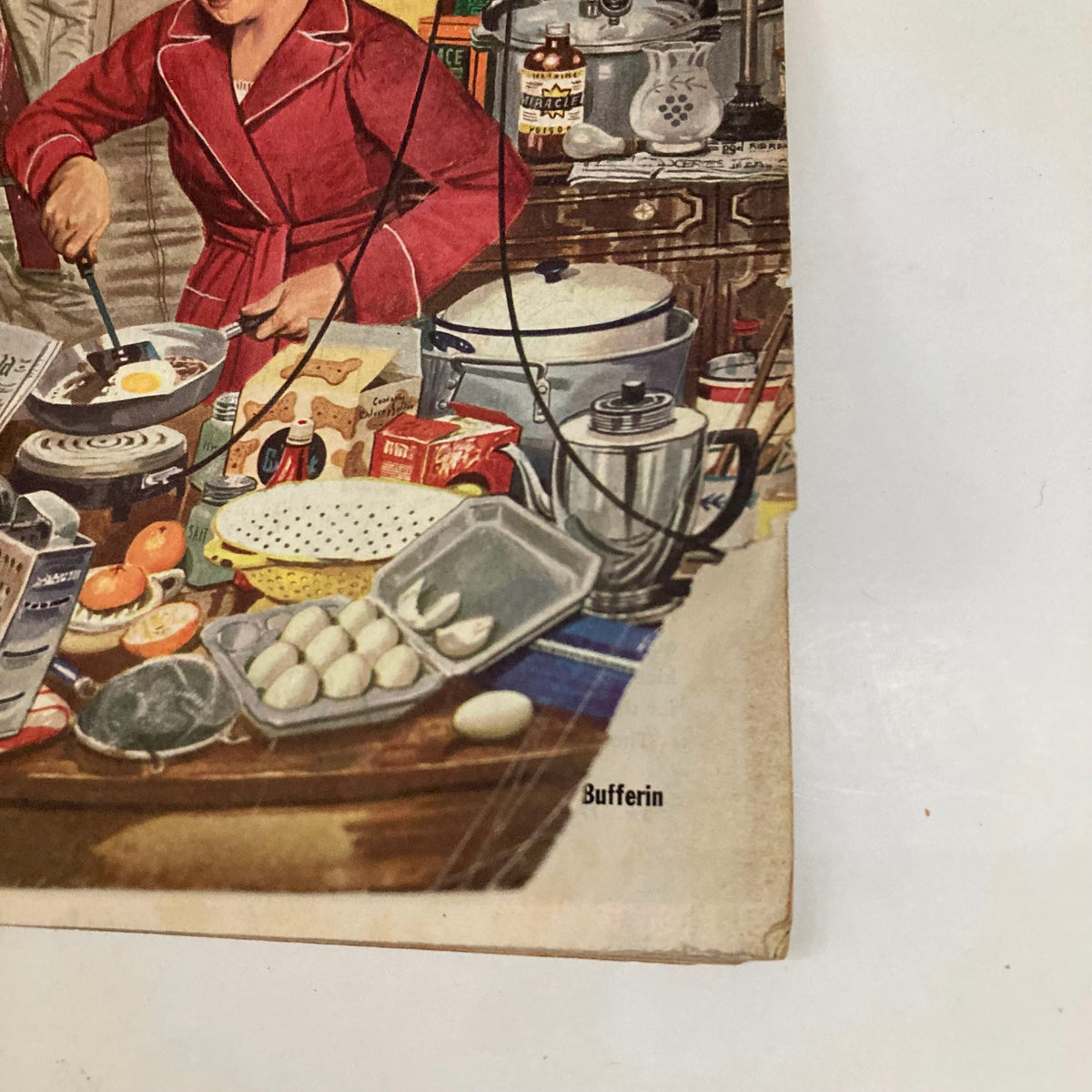 Interior view of a kitchen scene from the Saturday Evening Post Magazine, December 3, 1953, showcasing a woman frying eggs and a busy table filled with food items and kitchenware.