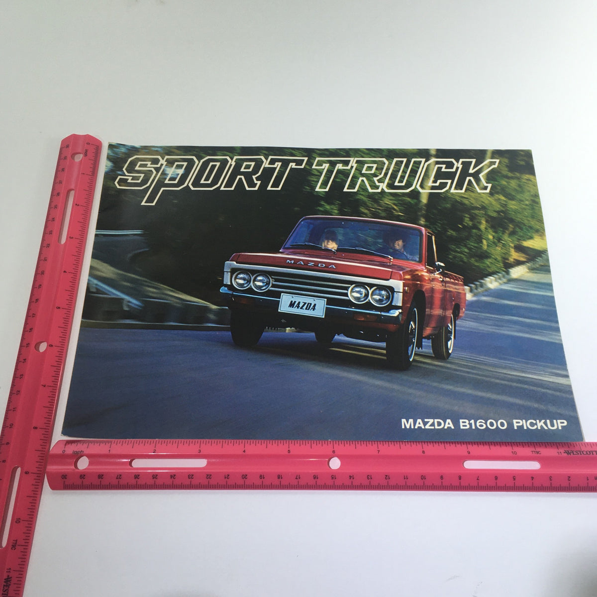 1975 Mazda B1600 Pickup Sport Truck brochure cover featuring a red Mazda B1600 Pickup driving on a scenic road, showcasing the sporty design and style of this classic auto brochure catalog.