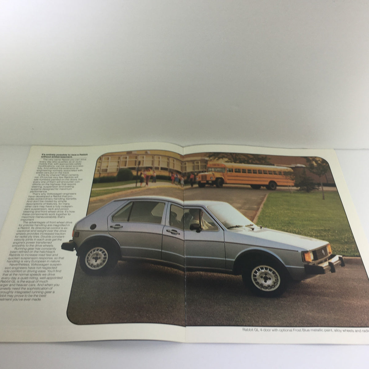 Inside view of the 1983 Volkswagen Rabbit GTI GL Dealership Car Auto Brochure Catalog displaying a silver Rabbit GL model alongside a school bus in the background.