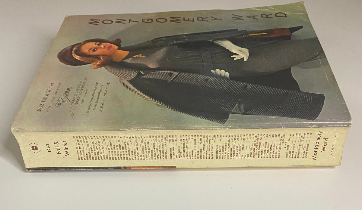 Side view of the 1962 Montgomery Ward Fall and Winter Catalog displaying the cover and spine, highlighting vintage fashion advertising and designer collections.