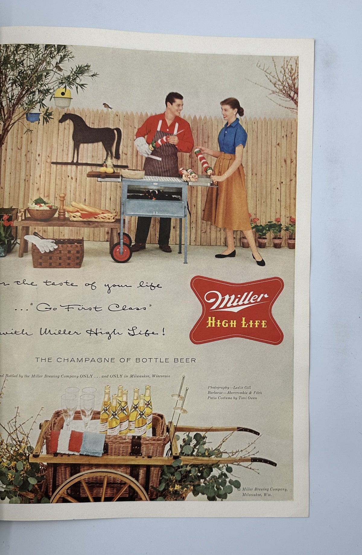 Vintage advertisement for Miller High Life beer showcasing a couple grilling outdoors, with the slogan 'THE CHAMPAGNE OF BOTTLE BEER.' Featured in Esquire Magazine May 1956.