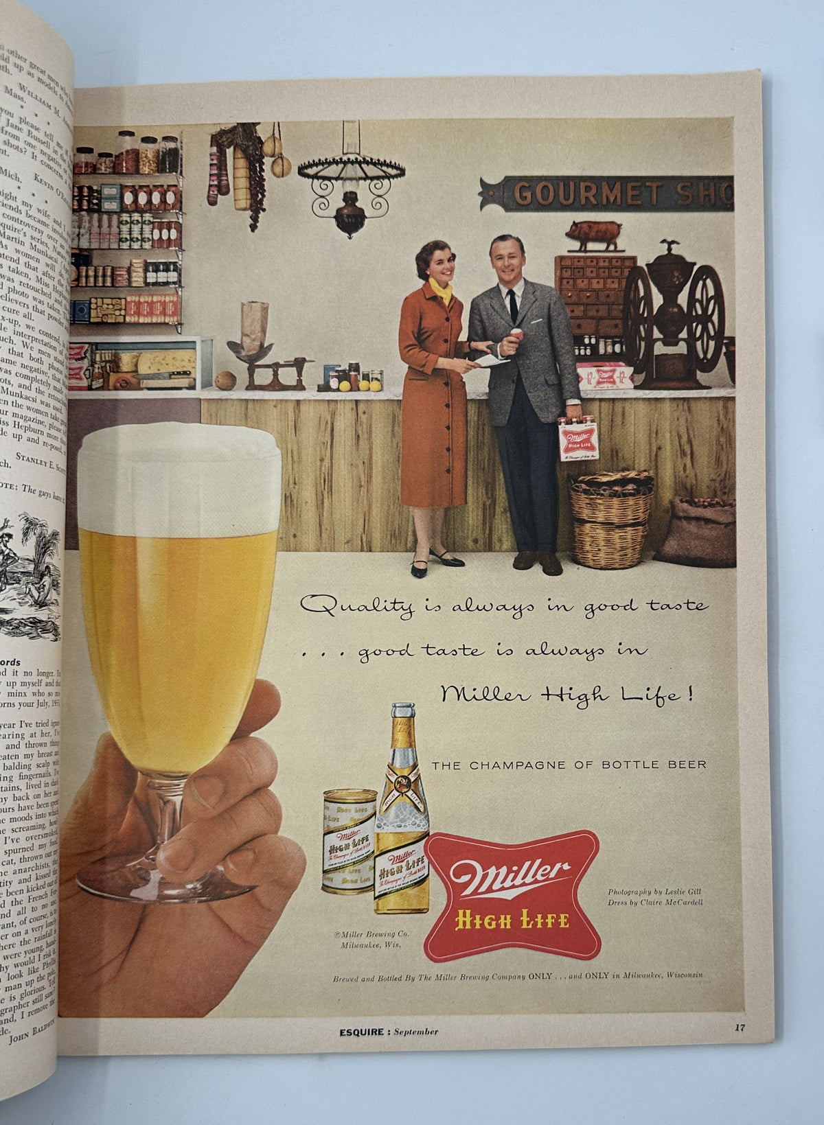 Esquire Magazine September 1956 advertisement featuring a couple in a gourmet shop promoting Miller High Life, with a hand holding a glass of beer in the foreground.