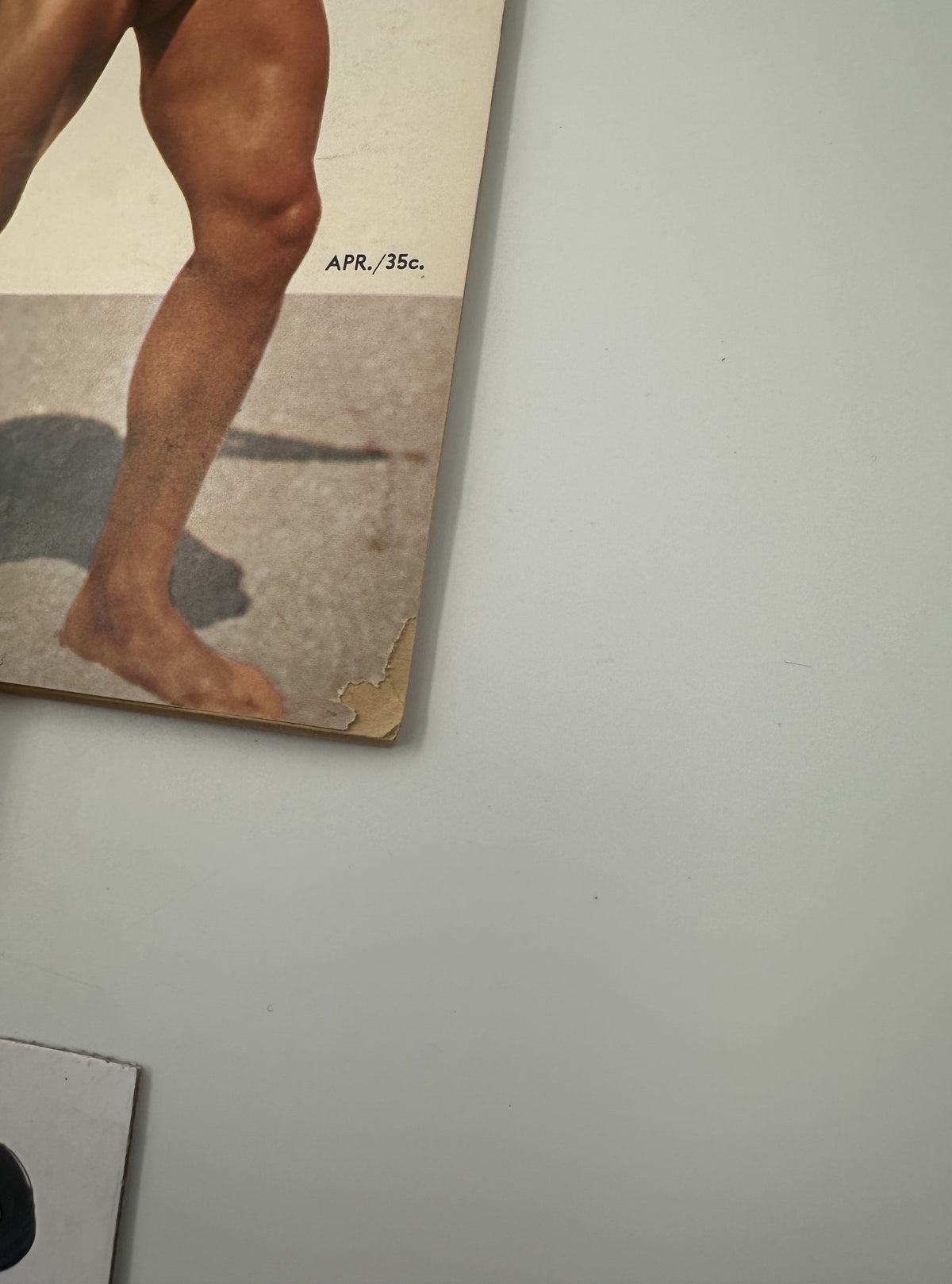 Close-up of the bottom corner of the Muscle Power Magazine April 1955, showing wear with a torn edge, highlighting the magazine's age and historic value.