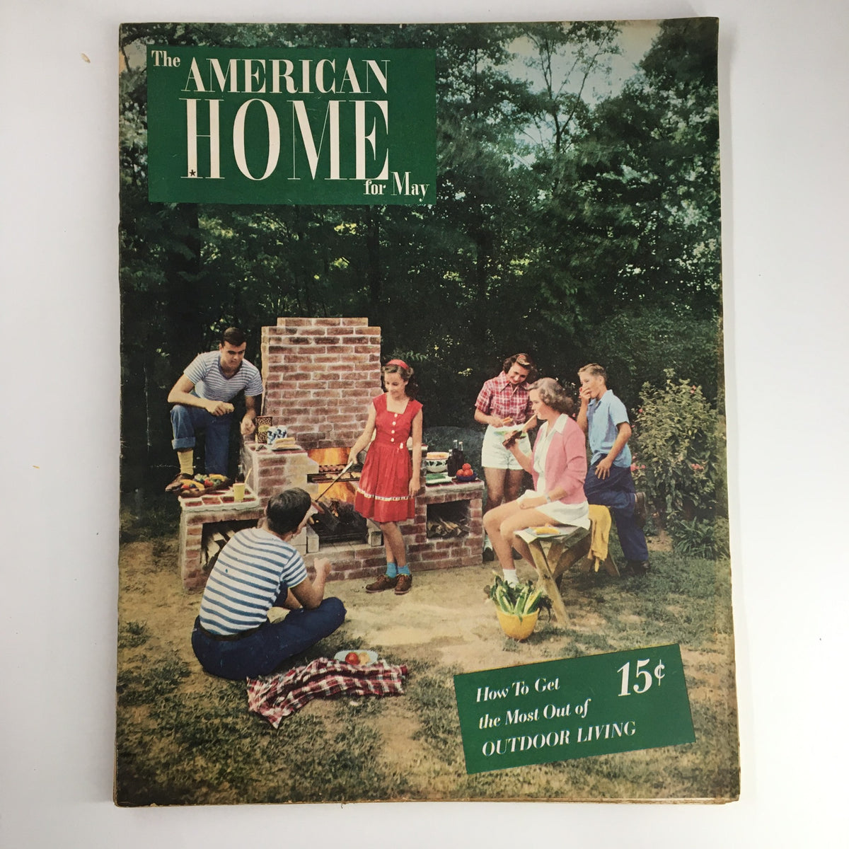 Cover of 'VTG The American Home May 1947' magazine featuring a lively outdoor gathering with a barbecue and friends enjoying nature.