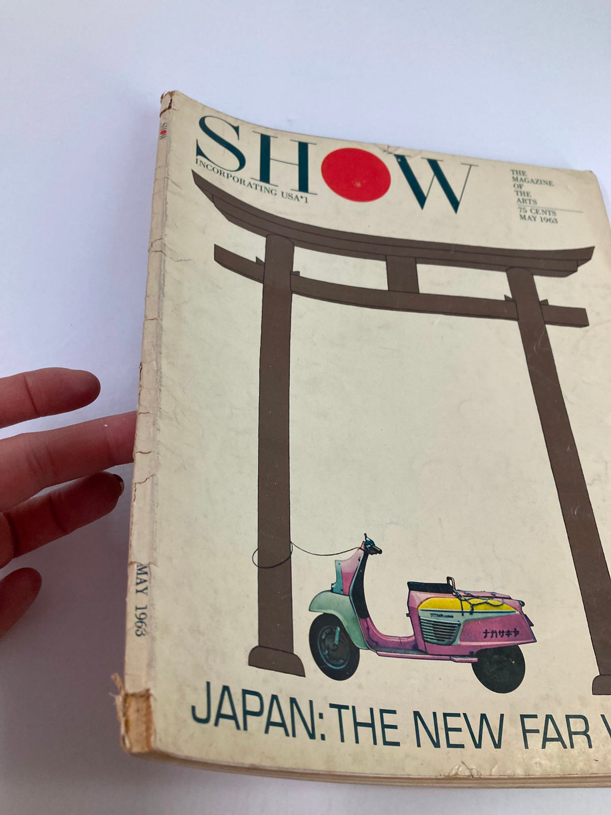 Side view of the VTG Show Magazine of the Arts May 1963, showcasing the cover art with a Torii gate and scooter, captured in hand.