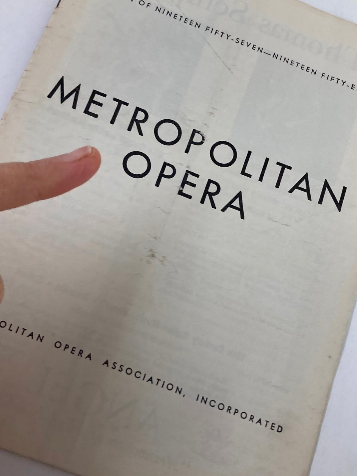 Close-up of the 1958 Metropolitan Opera Program cover emphasizing the title 'METROPOLITAN OPERA,' with a finger pointing to the text, illustrating the program's vintage nature and collectible appeal.