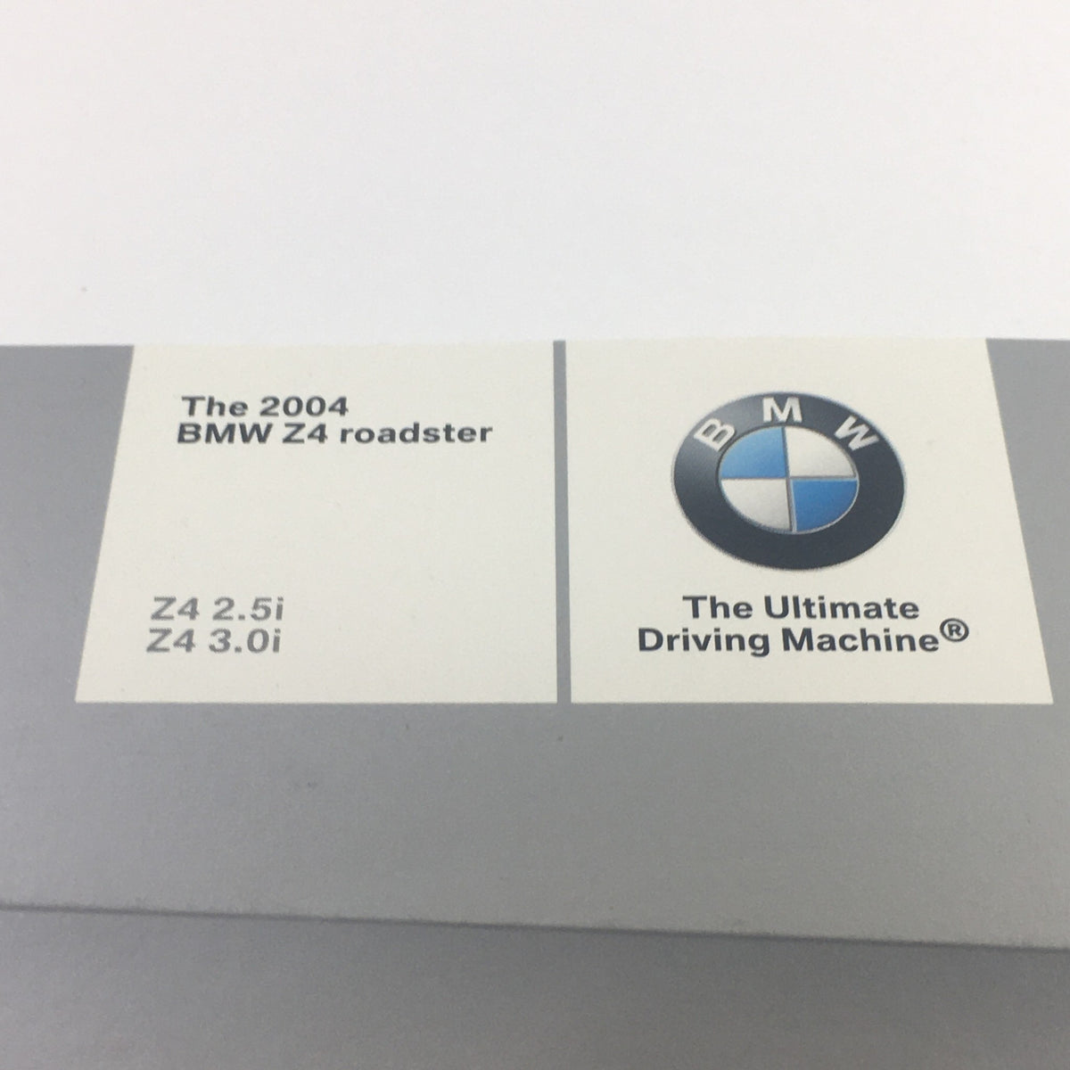 Close-up of the 2004 BMW Z4 Roadster 2.5i 3.0i Dealership Car Auto Brochure label, showcasing the BMW logo and model details.