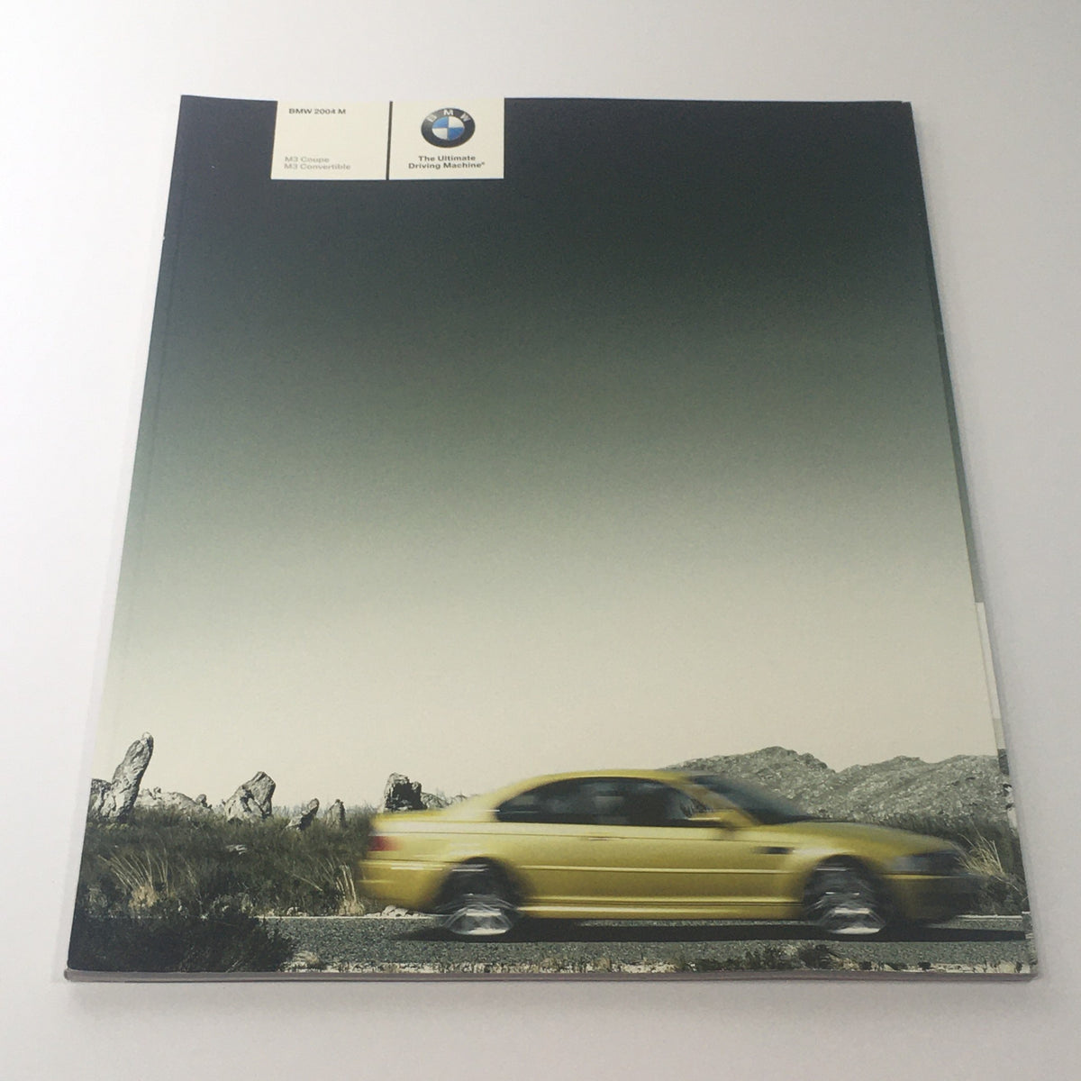 2004 BMW M3 Coupe - Convertible Dealership Car Auto Brochure Cover featuring a yellow BMW M3 driving through a scenic road.