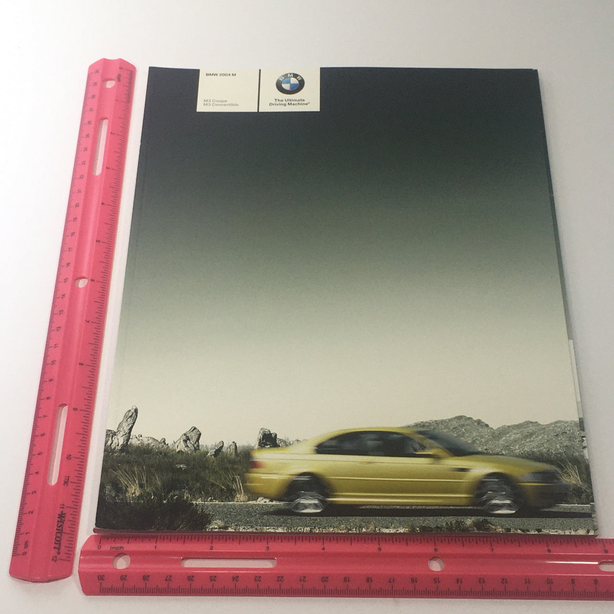2004 BMW M3 Coupe - Convertible Dealership Car Auto Brochure Catalog highlighting the front cover with a yellow BMW M3 on a scenic route, showcasing the brochure's sleek presentation.