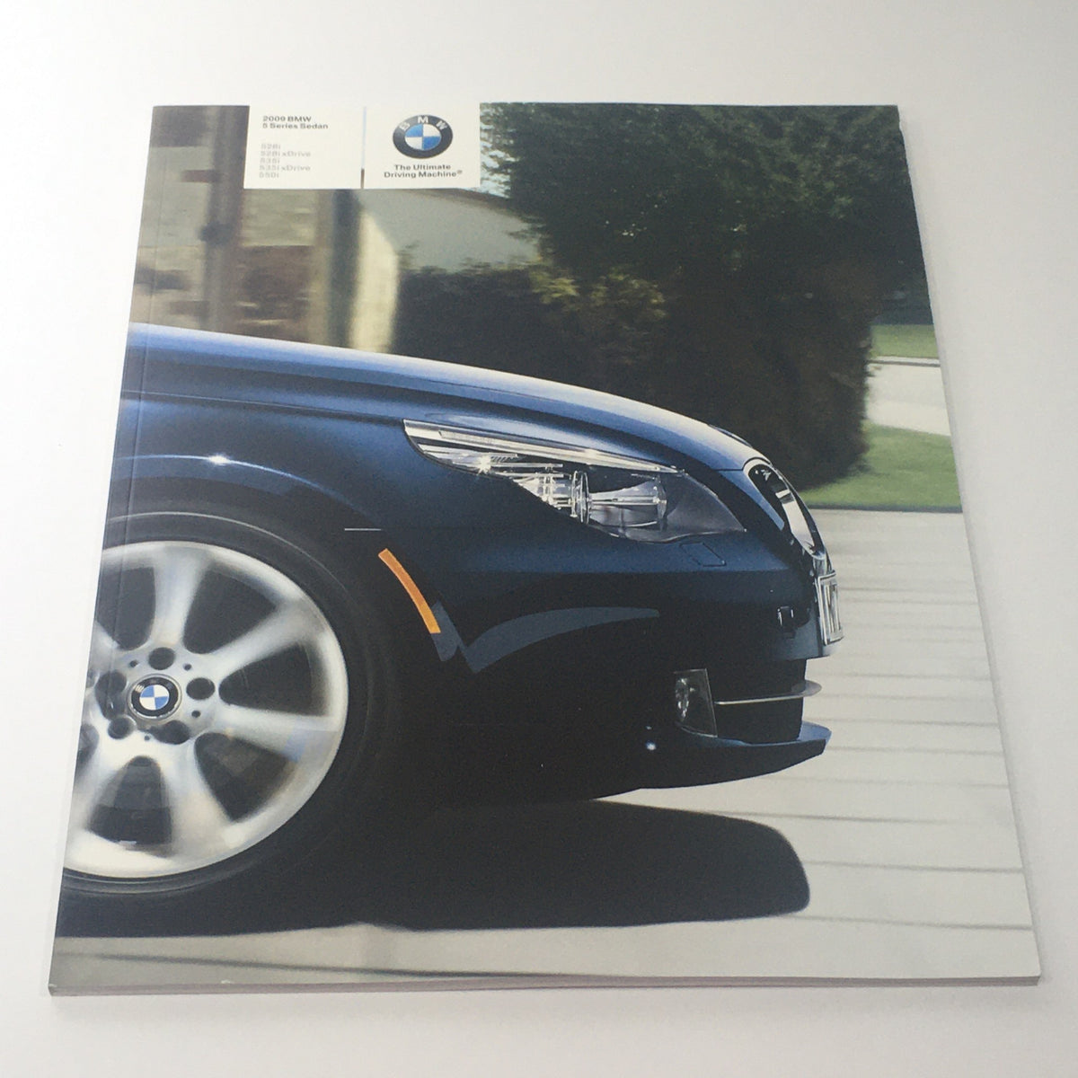 2009 BMW 5 Series Sedan brochure featuring the front profile of a blue BMW car with a sleek design on a driveway.