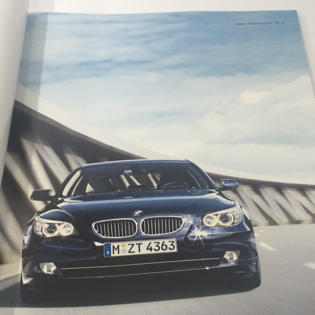 Image from the 2009 BMW 5 Series Sedan brochure showcasing a blue BMW car driving on a highway, emphasizing its luxury and performance.