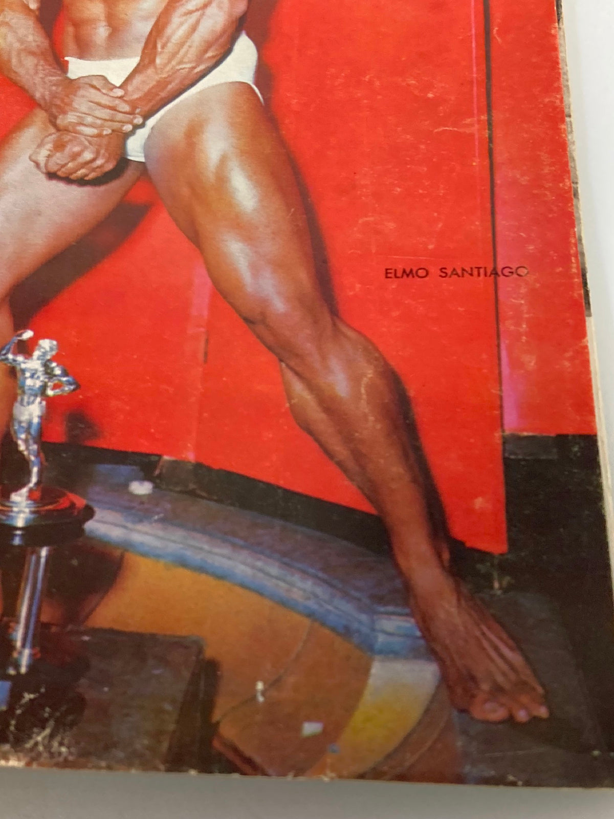 Detailed view of the lower section of the VTG Muscular Development Magazine February 1966 Vol 3 #2 cover, displaying Elmo Santiago's muscular leg, showcasing vintage bodybuilding aesthetics.