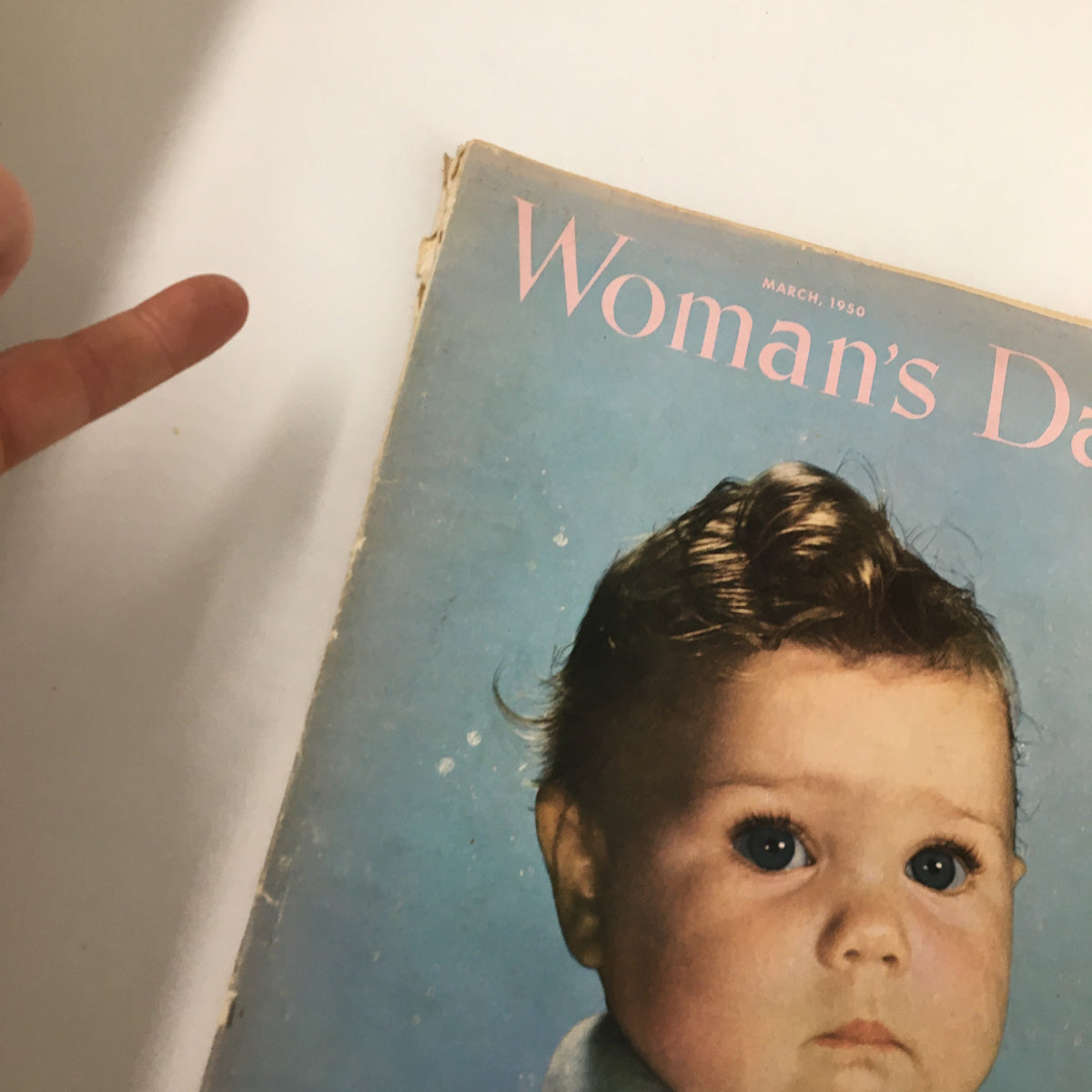 Close-up of the Vintage Woman's Day Magazine March 1950 cover showing a baby and part of a finger pointing towards the magazine.