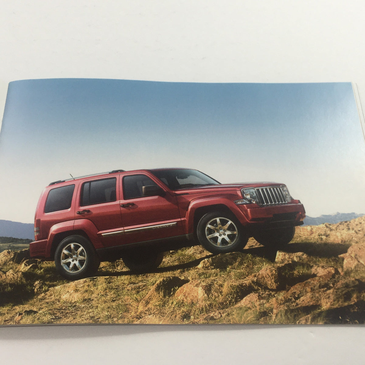 Image from the 2008 Jeep Compass Patriot Liberty Wrangler Dealership Car Auto Brochure Catalog depicting a red Jeep vehicle on rugged terrain.
