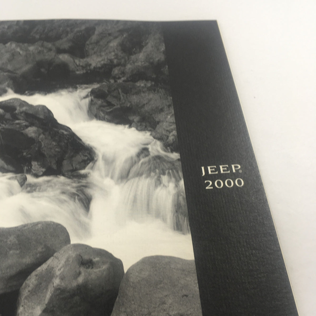 Close-up view of the cover of the 2000 Jeep Cherokee, Grand Cherokee Wrangler Dealership Car Auto Brochure Catalog featuring flowing water and rocky textures.
