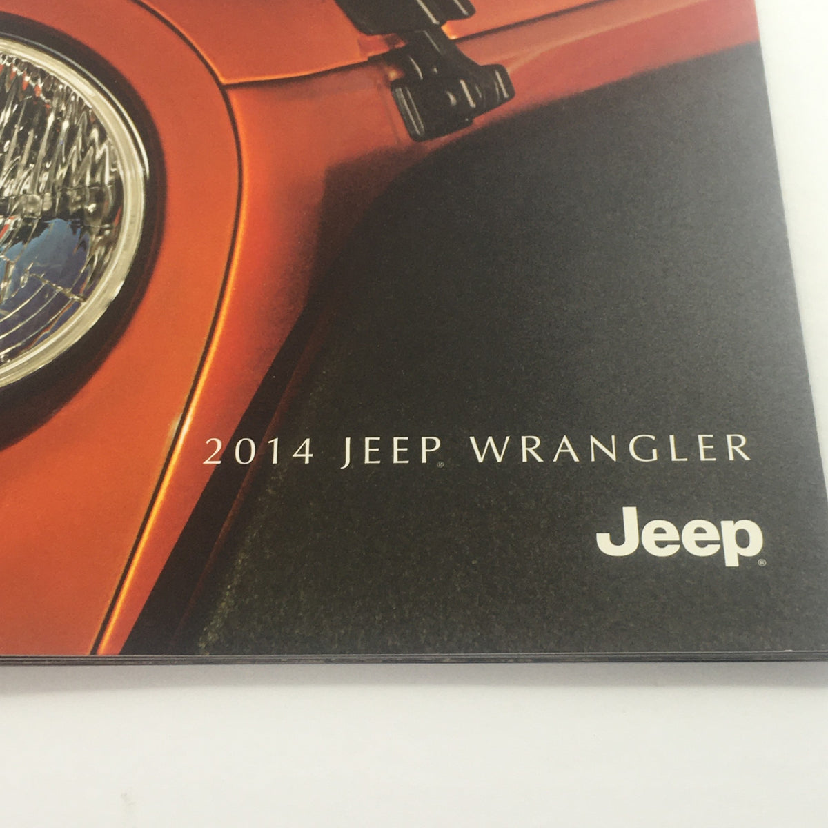 Detail shot of the 2014 Jeep Wrangler 4x4 Dealership Car Auto Brochure Catalog highlighting the Jeep logo and headlight design.