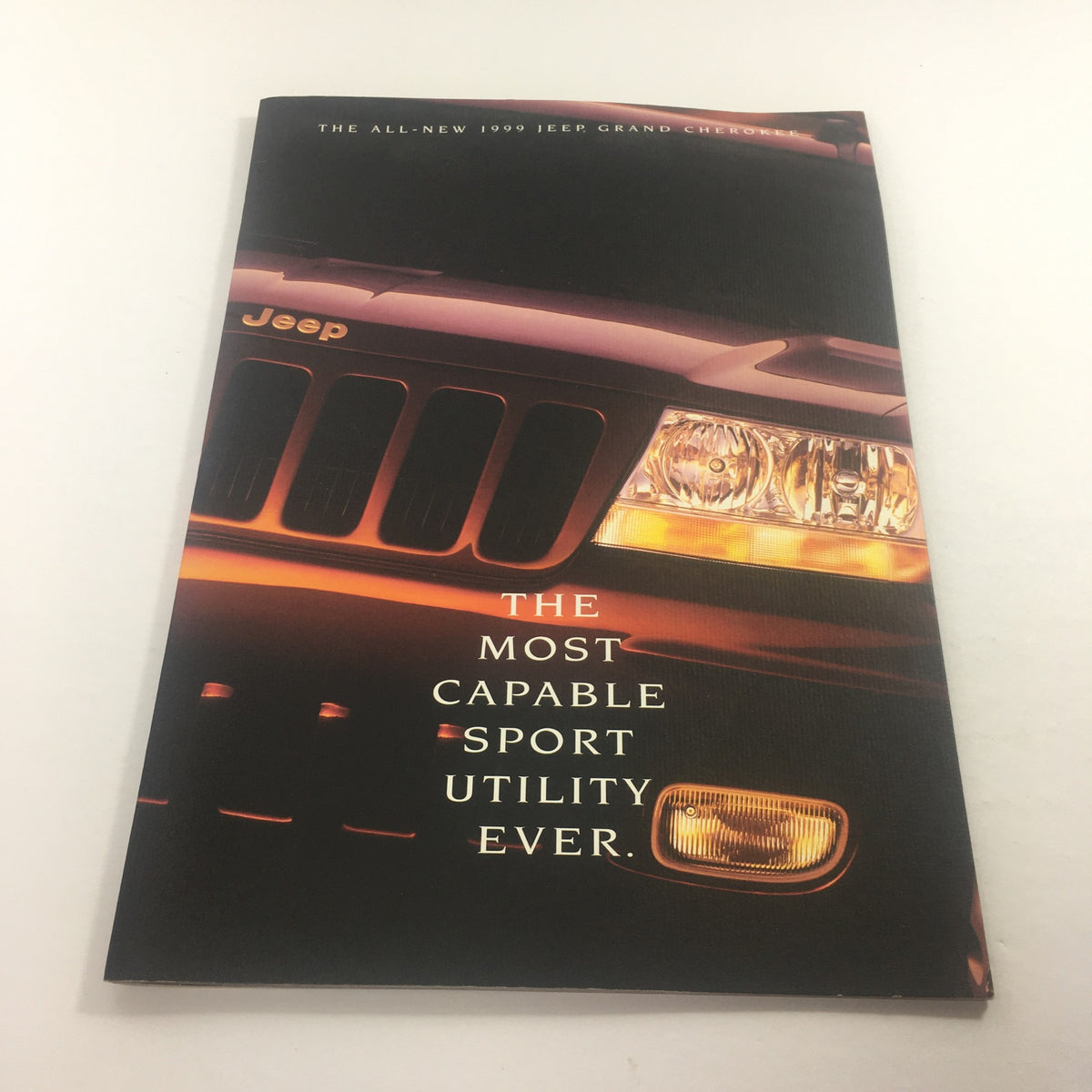 Cover of the 1999 Jeep Grand Cherokee SUV Dealership Car Auto Brochure Catalog showcasing the vehicle's sleek front design and highlighting its capabilities.