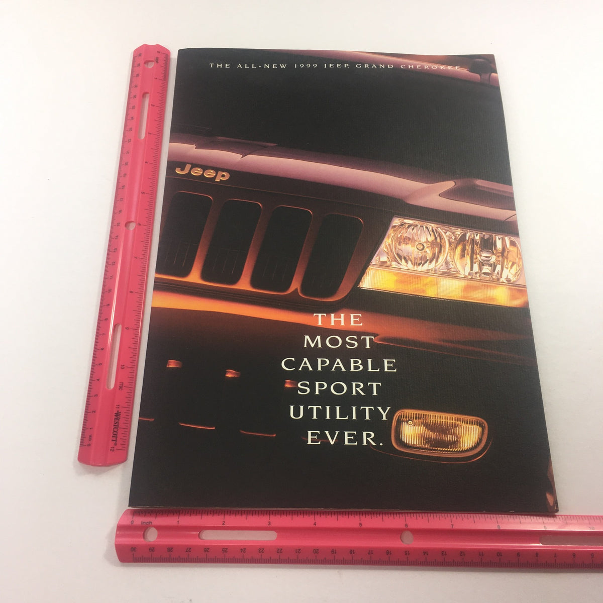Side view of the 1999 Jeep Grand Cherokee SUV Dealership Car Auto Brochure Catalog with a ruler for size reference, showcasing its professional design.