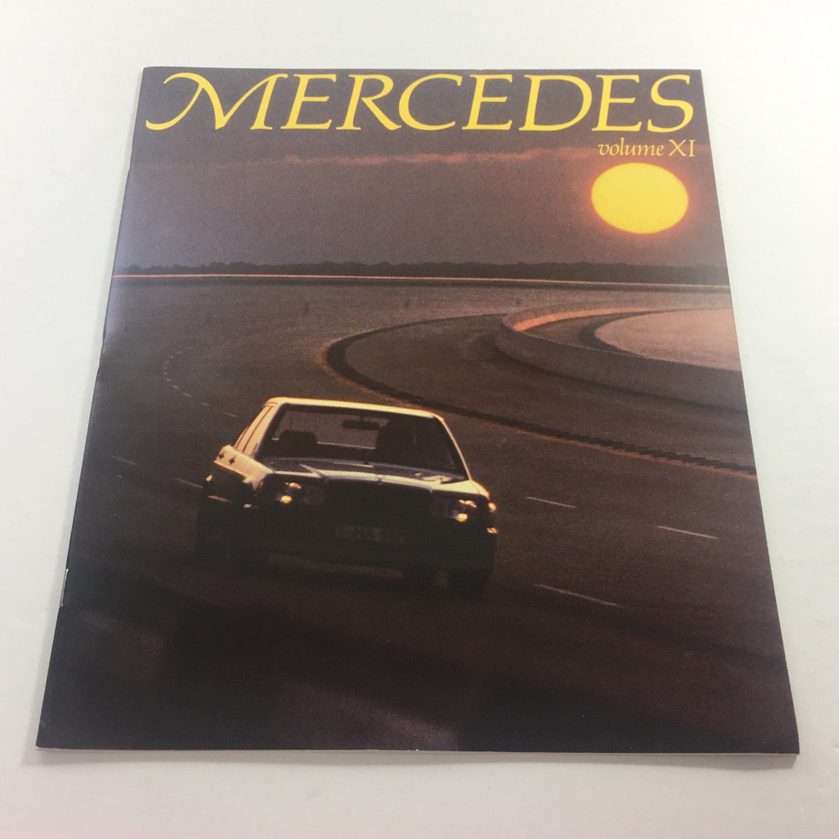 Cover image of the 1983 Mercedes Volume XI Dealership Car Auto Brochure Catalog featuring a Mercedes-Benz vehicle on a winding road at sunset.