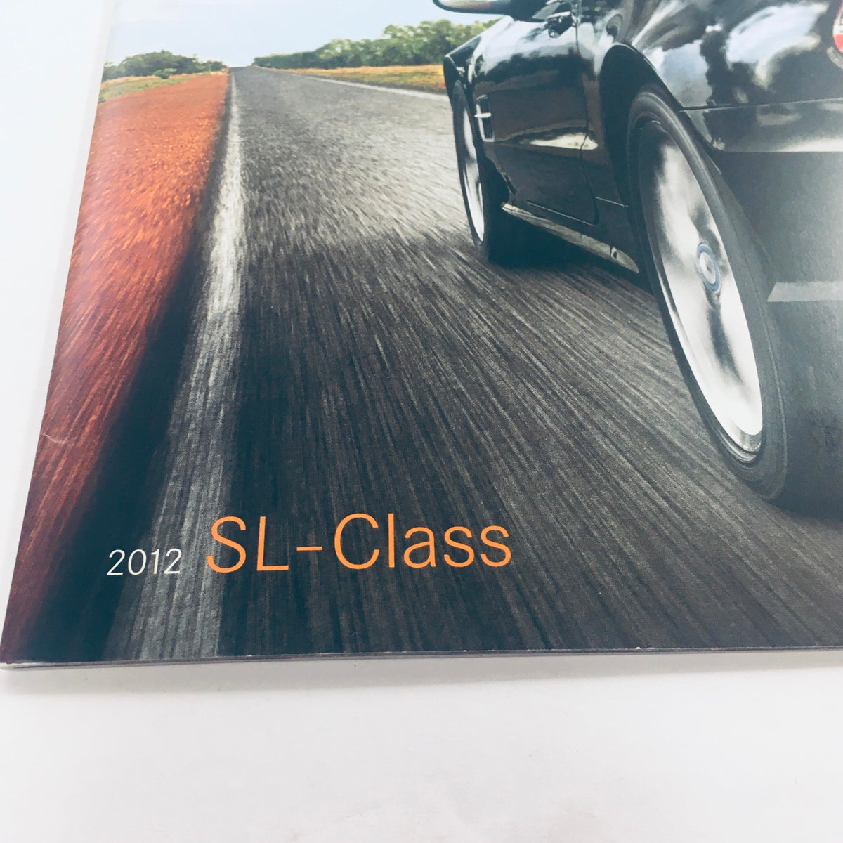 Close-up view of the 2012 Mercedes-Benz SL-Class Dealership Car Auto Brochure Catalog highlighting the SL-Class title overlaid on a road background.