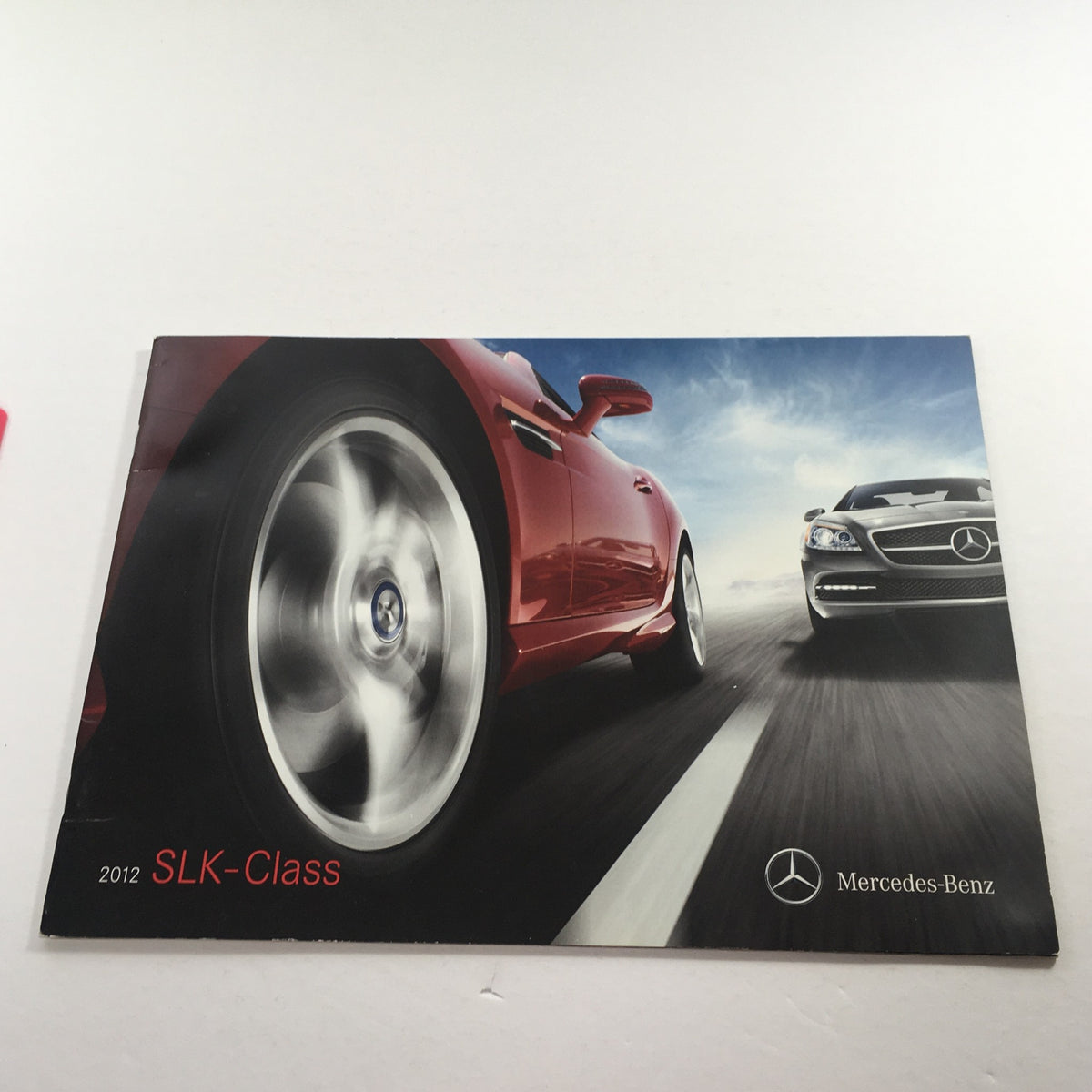 2012 Mercedes-Benz SLK-Class Dealership Car Auto Brochure Catalog featuring a dynamic image of a red SLK-Class in motion with a blurred background, showcasing the sporty design.
