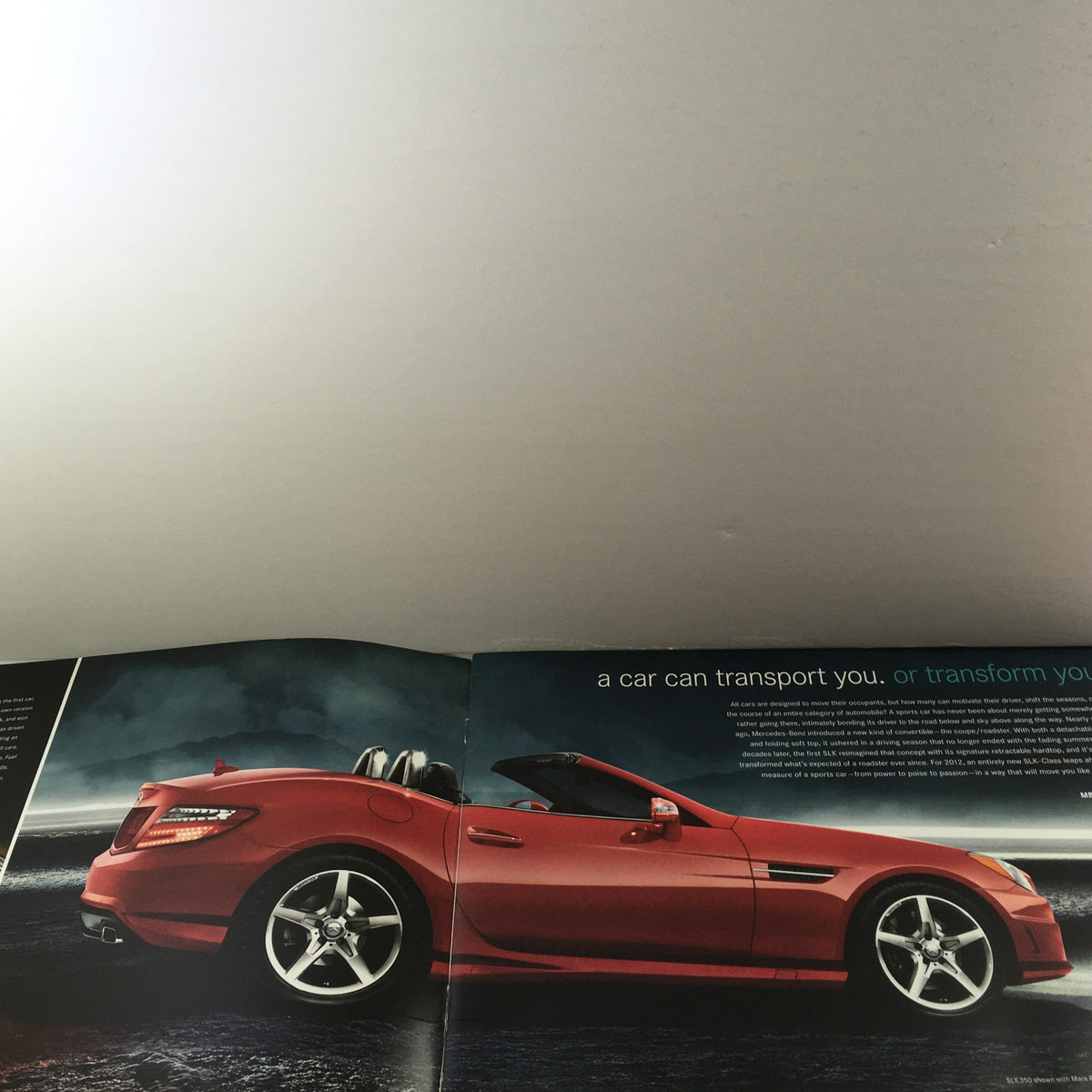Inside view of the 2012 Mercedes-Benz SLK-Class Dealership Car Auto Brochure Catalog showcasing a stylish red SLK-Class convertible parked in a dramatic scene, emphasizing luxury and performance.