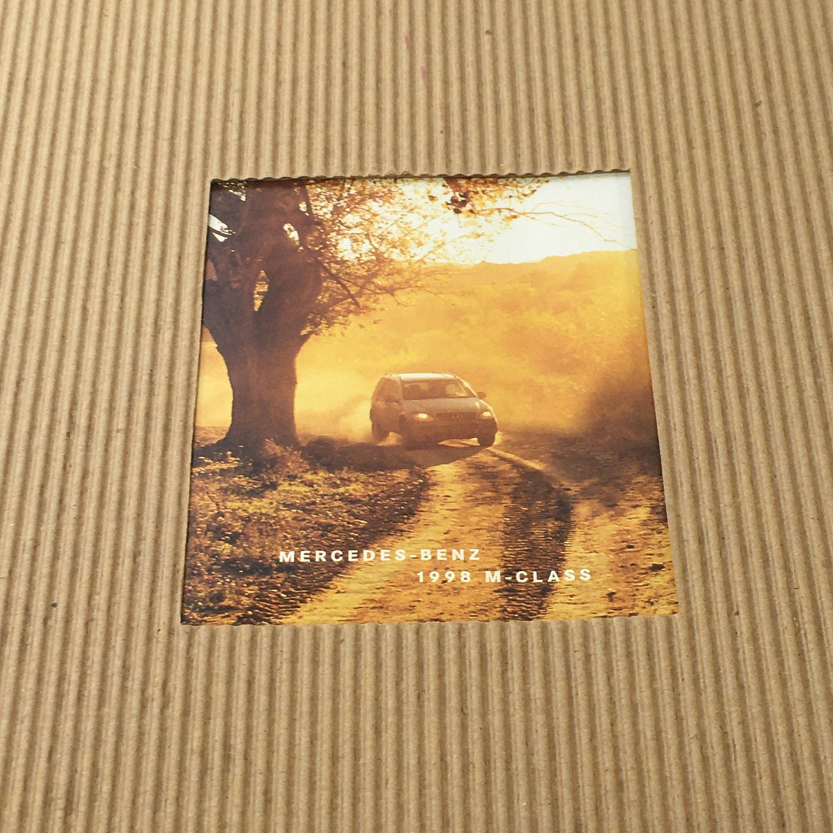 Detailed view of the 1998 Mercedes-Benz M-Class dealership car auto brochure catalog, showcasing an inset image of a vehicle surrounded by nature.