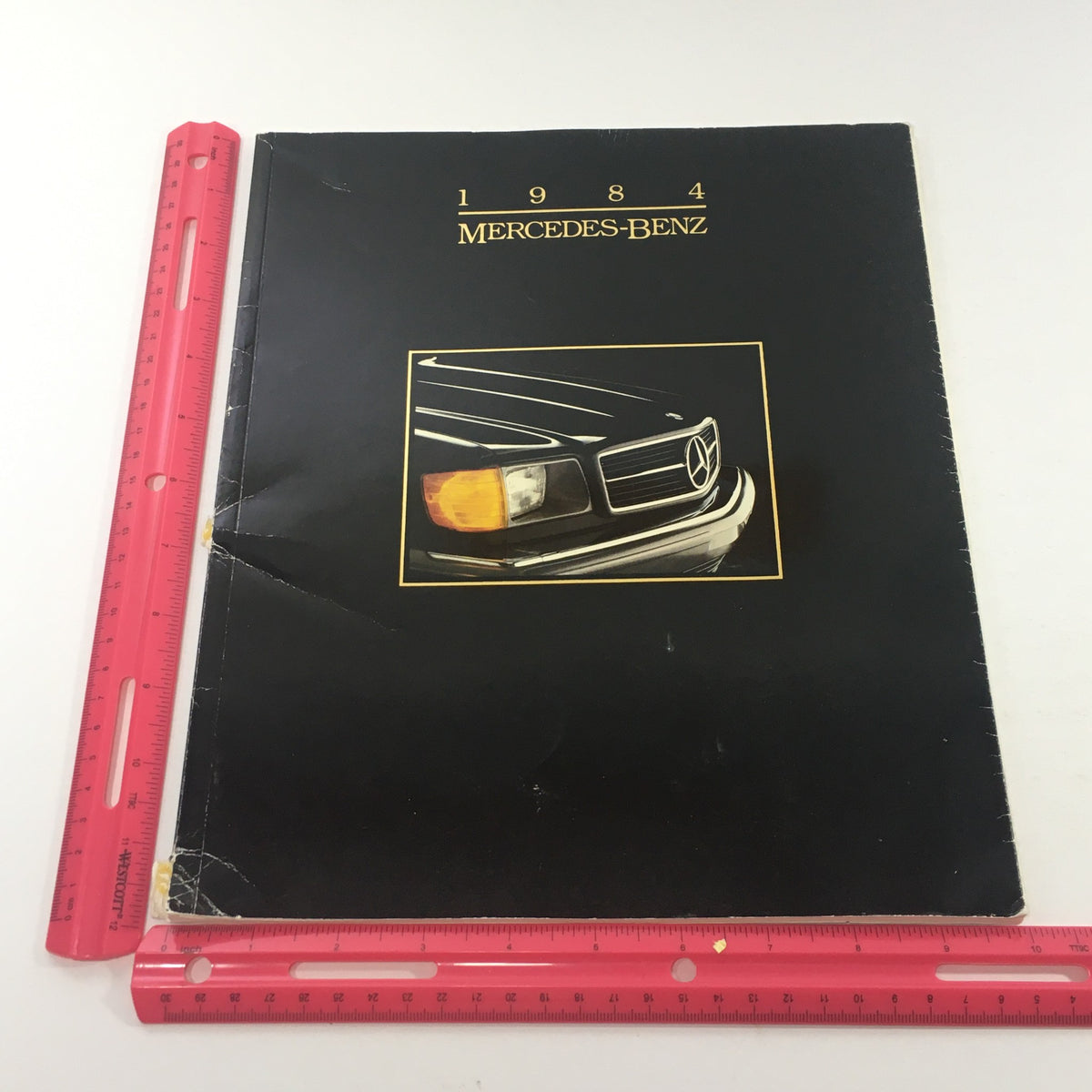 Front cover of the 1984 Mercedes-Benz 190E 2.3/190D 2.2 Sedans Dealership Car Auto Brochure Catalog with ruler for size reference.