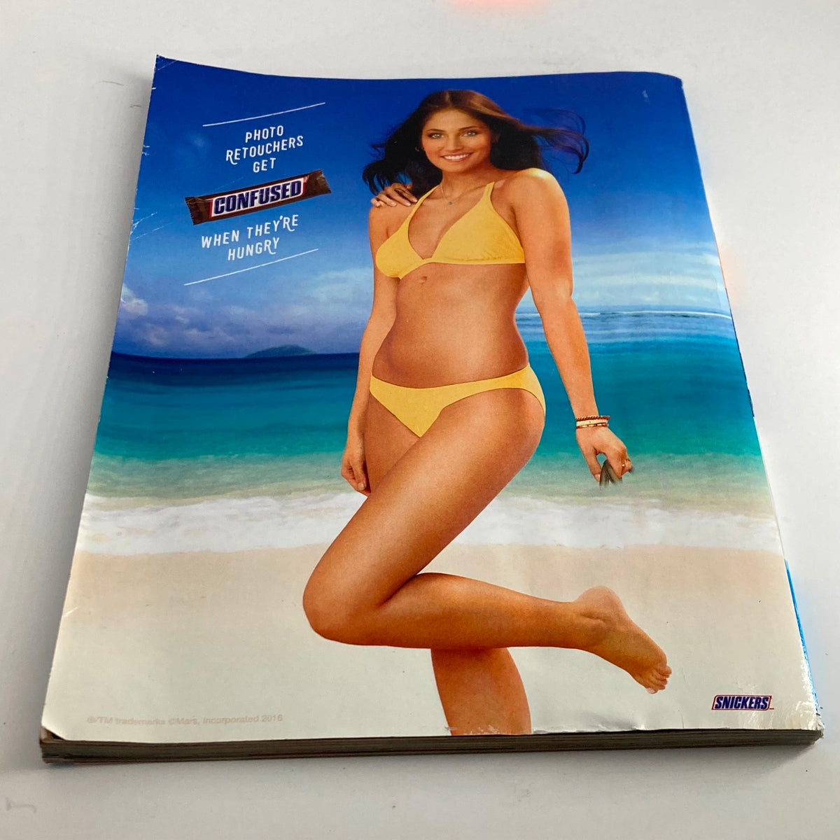 Back cover of the Sports Illustrated Magazine Winter 2016 Ashley Graham Swimsuit Issue displaying a model in a yellow bikini on the beach, representing the magazine's fun spirit.
