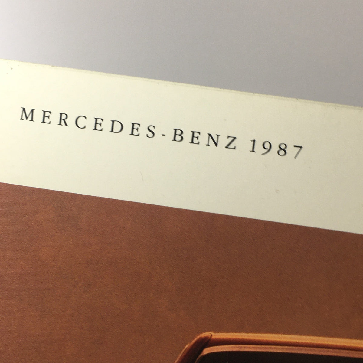Close-up of the 1987 Mercedes-Benz logo featured in the Full Model Line Dealership Car Auto Brochure Catalog.