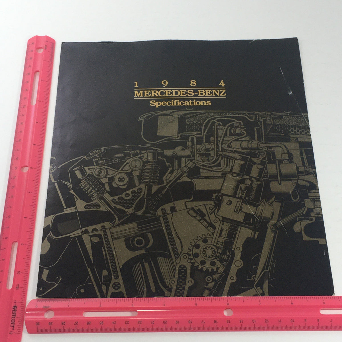 Cover of the 1984 Mercedes-Benz specifications brochure showcasing engine design and features, with a ruler for size reference.