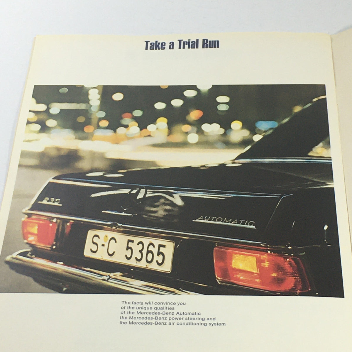 Interior page of the 1980s Mercedes-Benz AT/Power Steering Dealership Car Auto Brochure Catalog with a black Mercedes-Benz car and the phrase 'Take a Trial Run'.