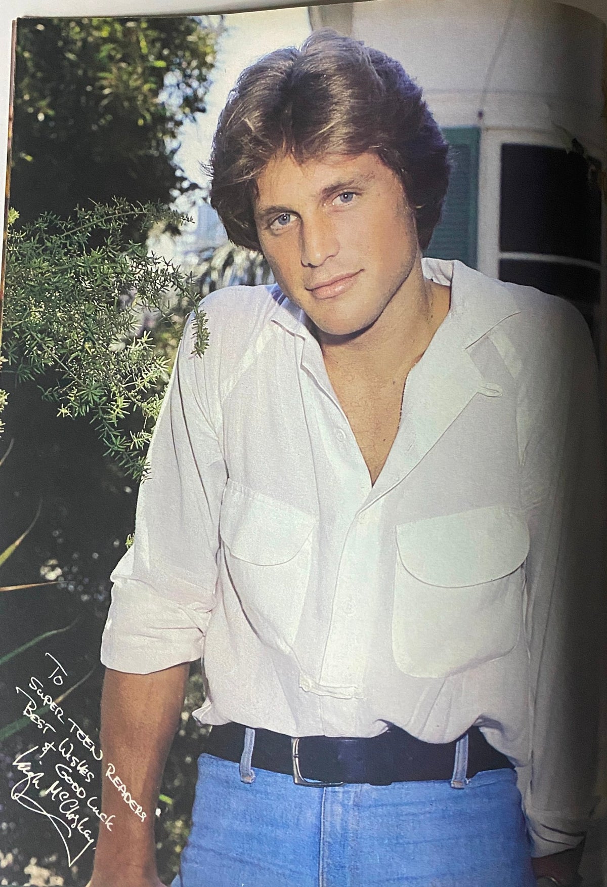 Full-body image of a male model wearing a white shirt and blue jeans, standing outdoors amidst greenery, featured in SuperTeen Magazine January 1981.