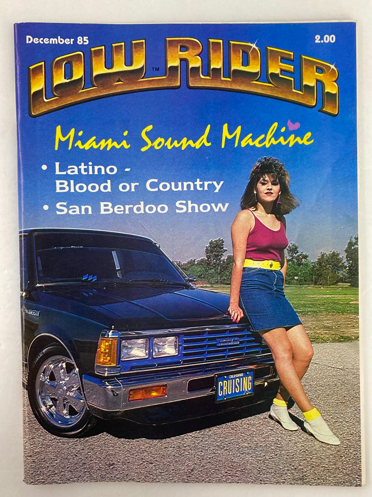 Cover of VTG LowRider Magazine December 1985 titled 'Miami Sound Machine' featuring a woman next to a lowrider vehicle, showcasing Latino culture and country influences.
