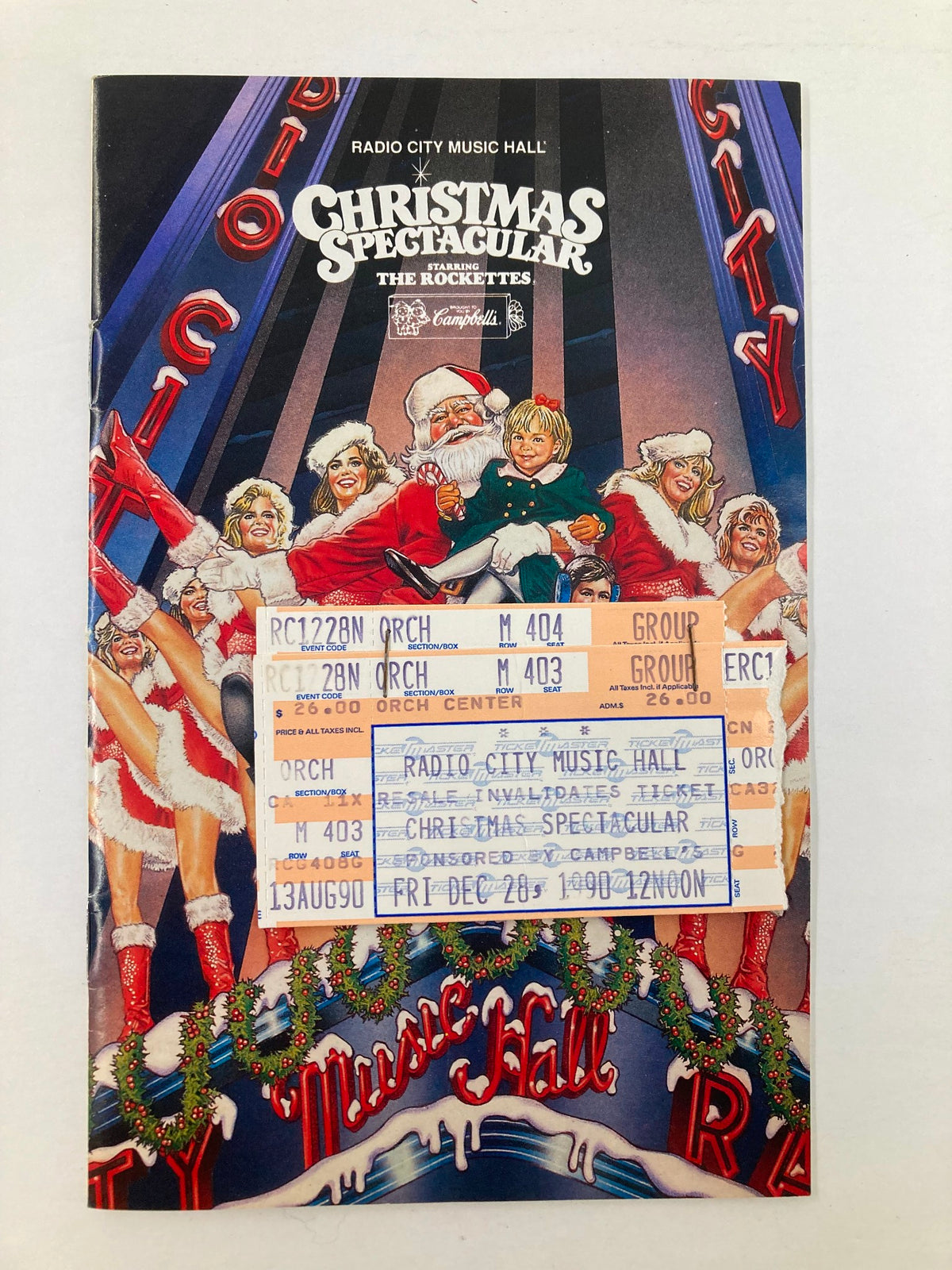 1990 Program Radio City Music Hall The Rockettes in Christmas Spectacular cover featuring Santa Claus, children, and holiday decorations, with ticket stubs attached.