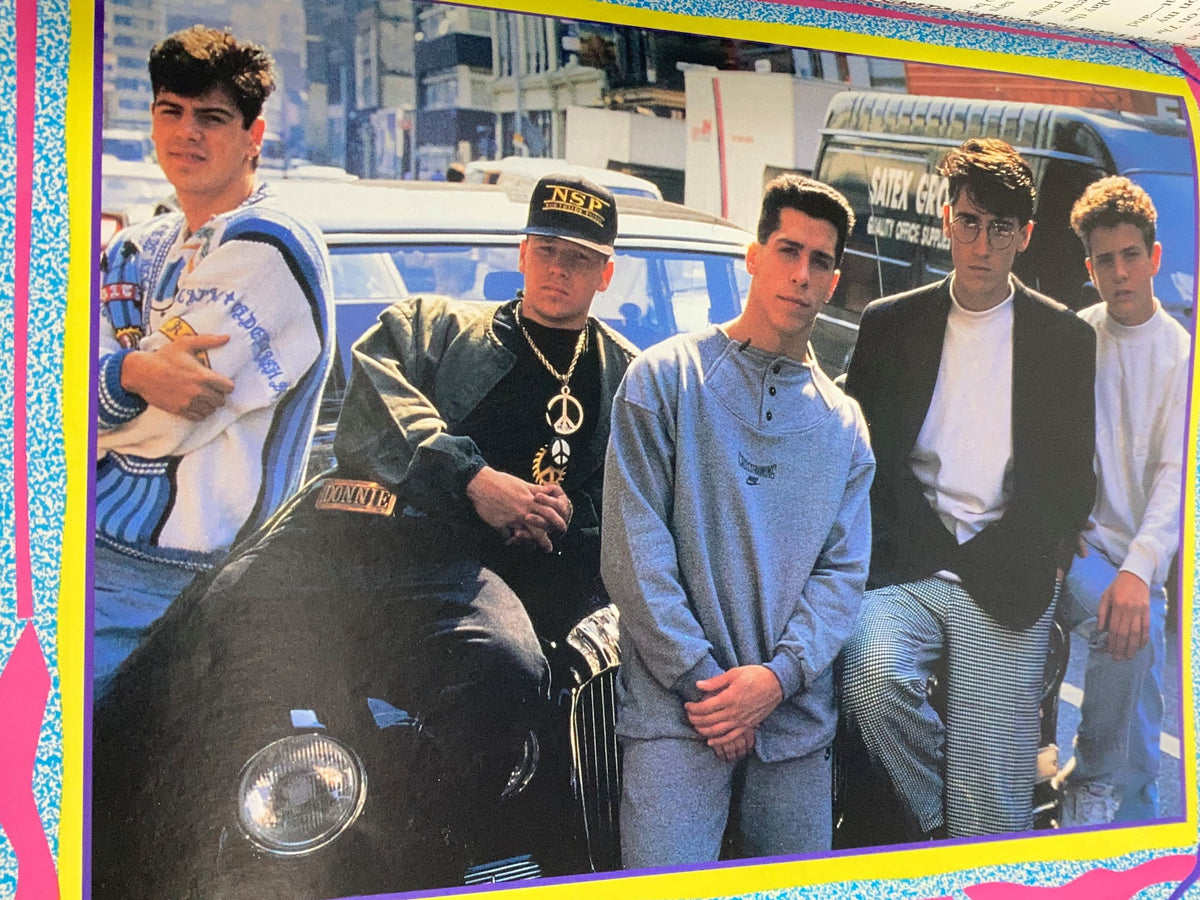 Band members of New Kids On The Block posing in front of a car in the '1990 New Kids On The Block Scrapbook by Grace Catalano'.