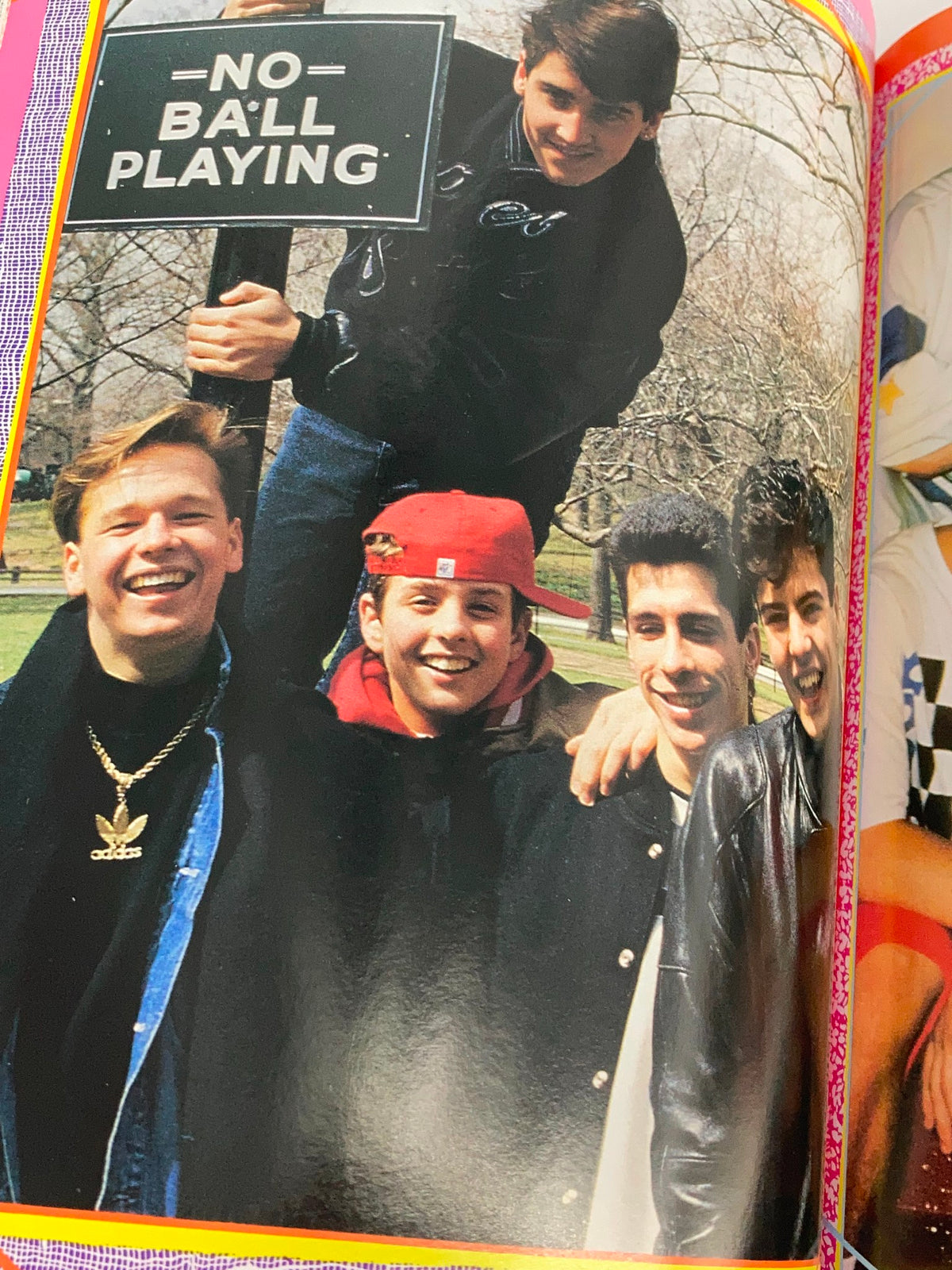 1990 New Kids On The Block Scrapbook by Grace Catalano, capturing a cheerful outdoor moment of the band members gathered under a 'No Ball Playing' sign, emphasizing their youthful vibe.