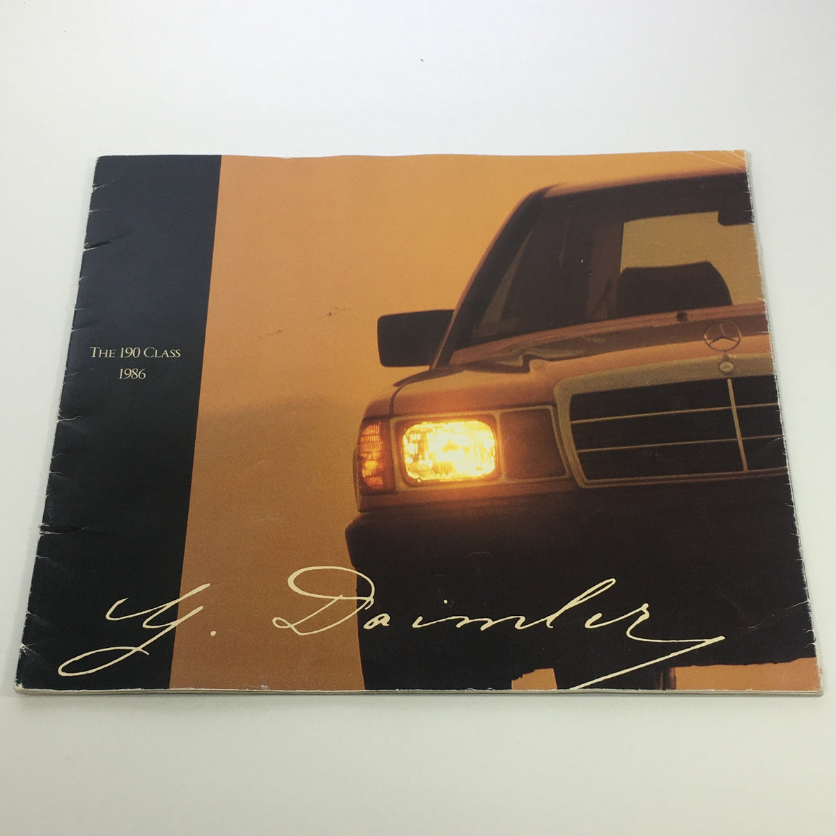 Cover of the 1986 Mercedes-Benz 190 Class Dealership Car Auto Brochure Catalog showcasing the vehicle's front and amber headlight against an elegant background.