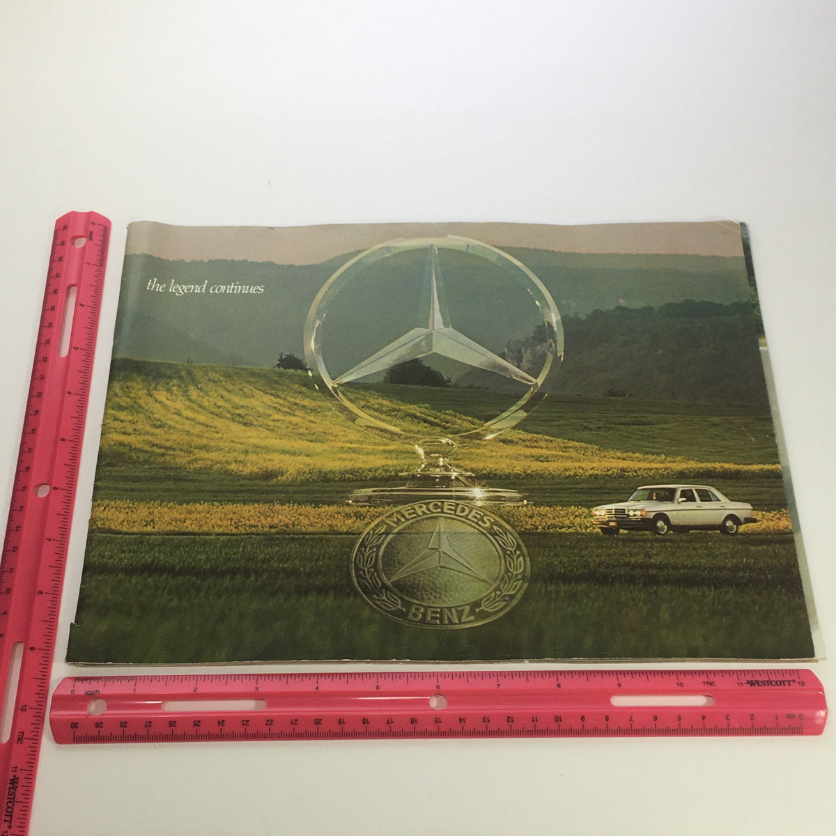 The front cover of the 1970s Mercedes-Benz 280SE 450SEL 450SL Dealership Car Auto Brochure Catalog, showcasing the iconic three-pointed star logo with a classic Mercedes-Benz vehicle in a scenic landscape.